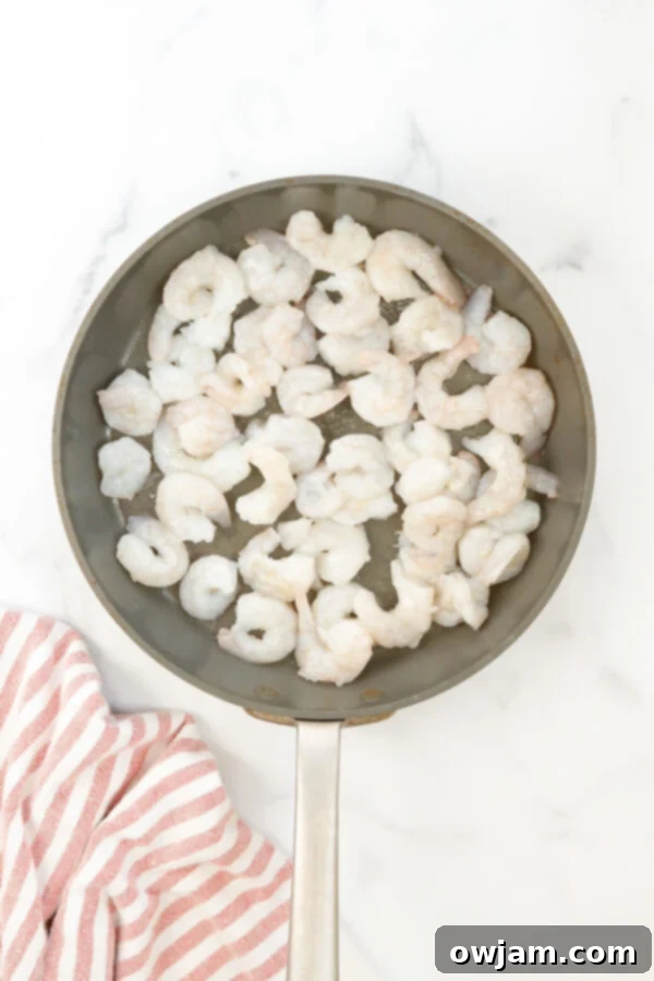Honey Garlic Sriracha Shrimp cooking in a hot skillet, with a few pieces already turning pink and curling.