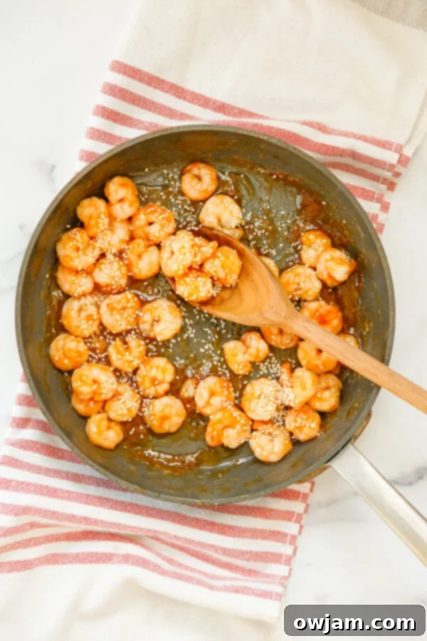 Honey Garlic Sriracha Shrimp simmering in a skillet, coated in a thick, glossy sweet and spicy sauce.