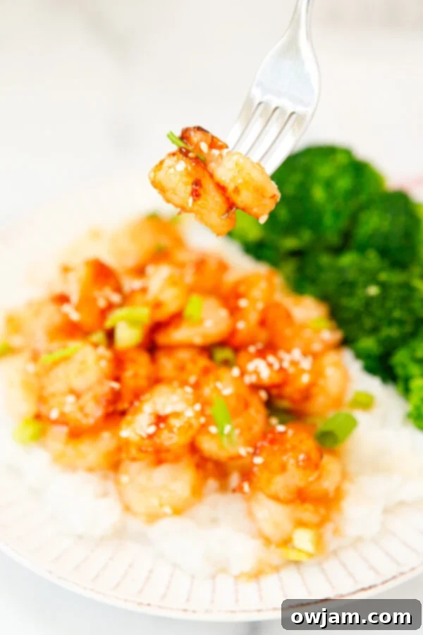 A fork piercing a piece of Honey Garlic Sriracha Shrimp, showcasing its tender texture and glossy coating.