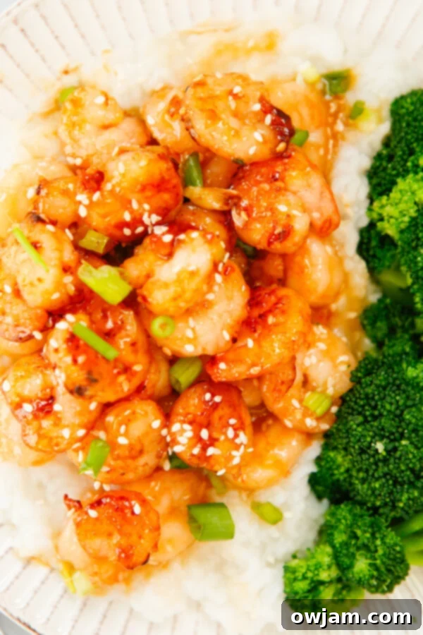 Honey Garlic Sriracha Shrimp in a bowl, generously garnished with sliced green onions and sesame seeds.
