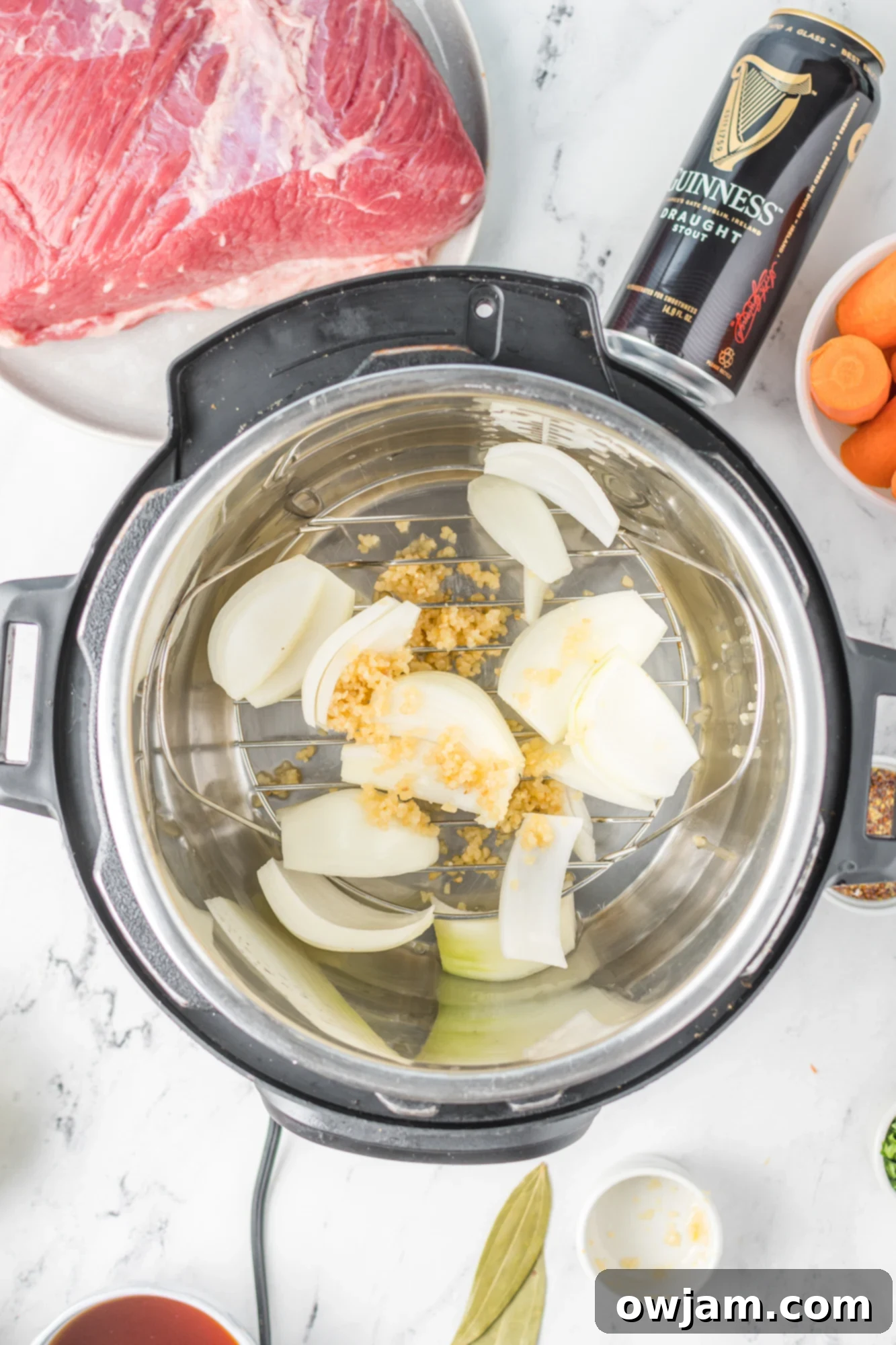 Tender Instant Pot Corned Beef and Cabbage 7 Onions, bay leaves, and garlic placed on the trivet in an Instant Pot for corned beef and cabbage