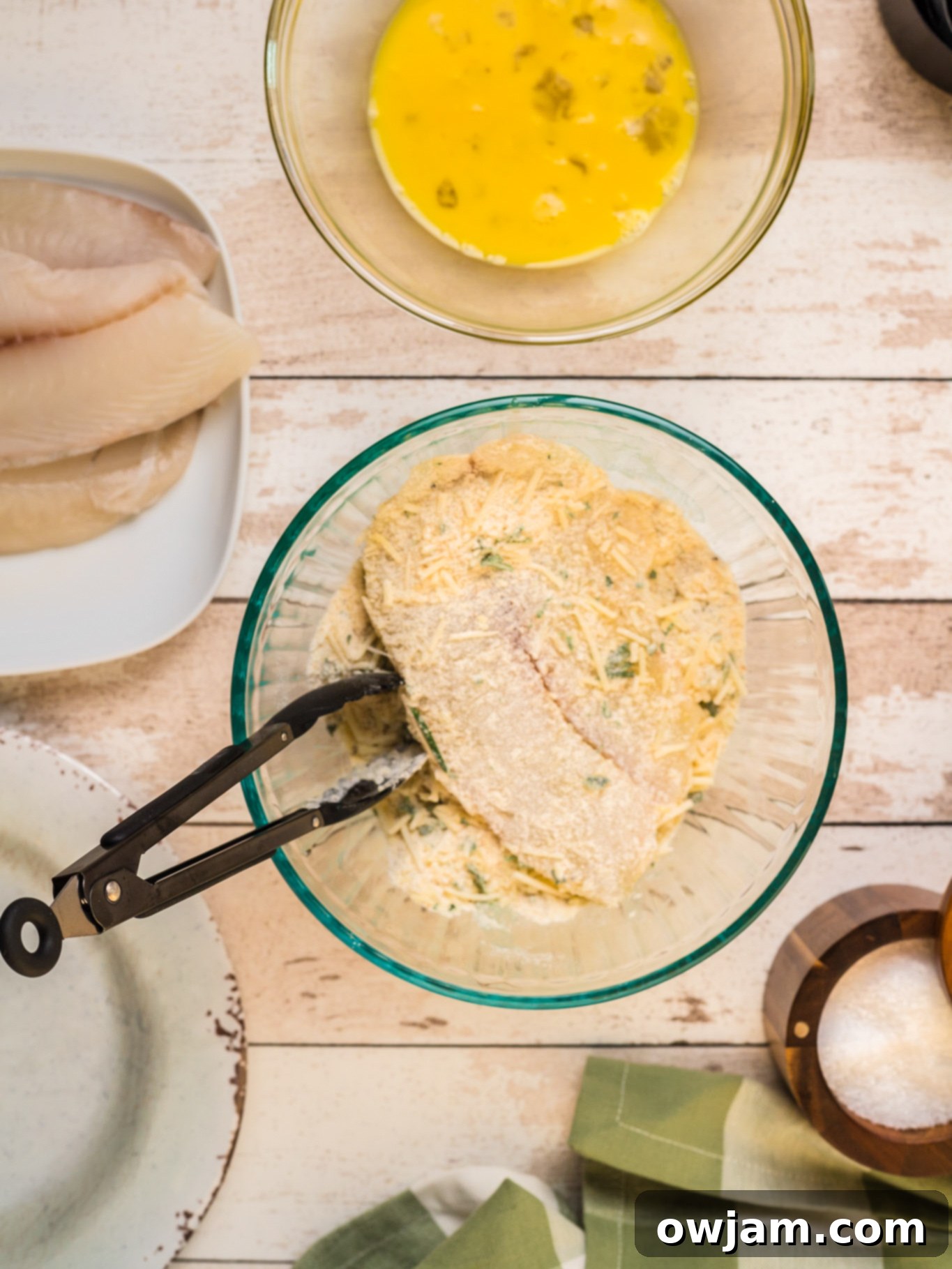 Crispy Parmesan Tilapia 7 Tilapia fillet being dipped in the egg wash with tongs, preparing it for the Parmesan breadcrumb coating.