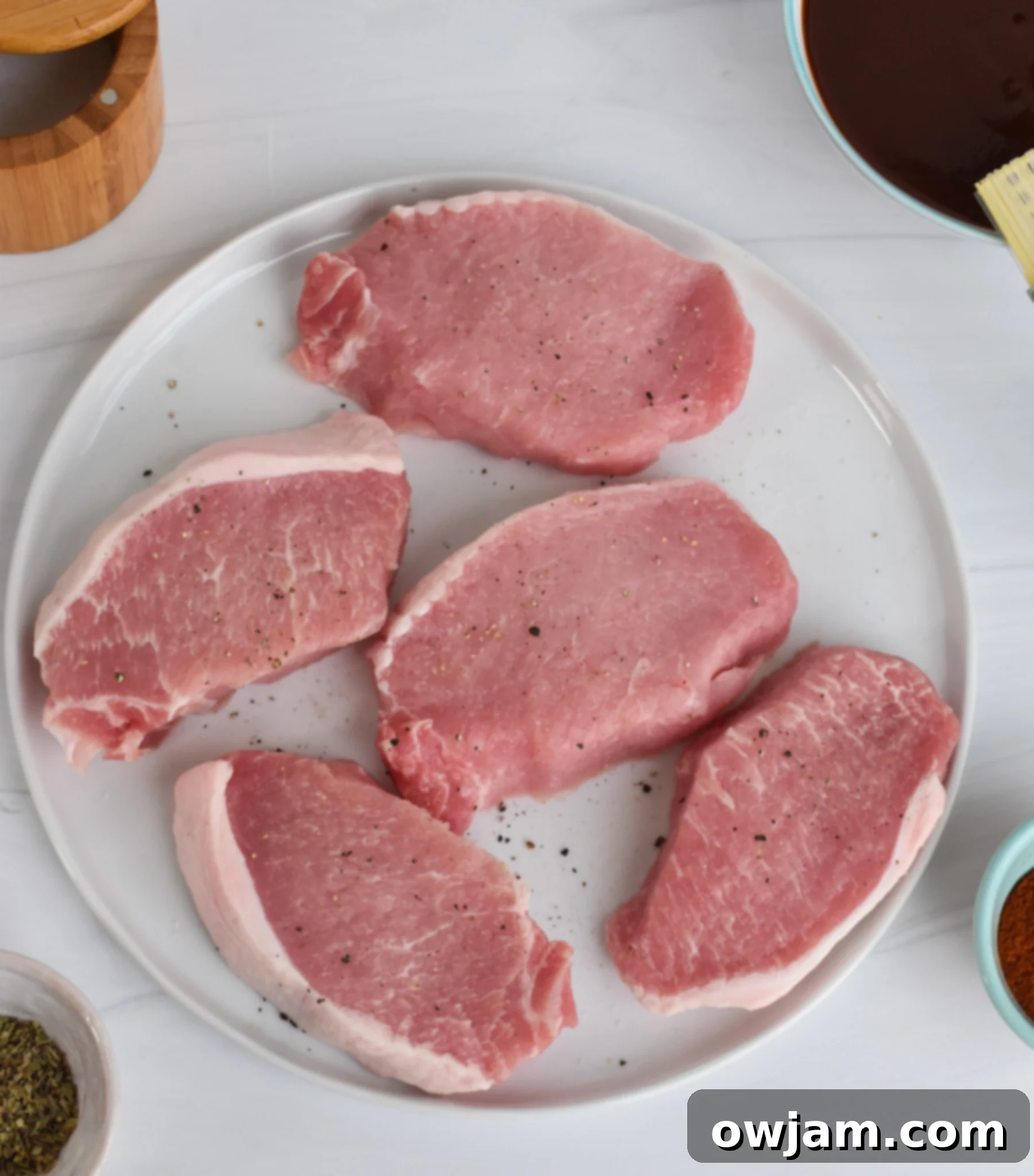 Mouthwatering BBQ Baked Pork Chops 3 All ingredients for BBQ Baked Pork Chops laid out on a wooden table: pork chops, spices, and BBQ sauce components.