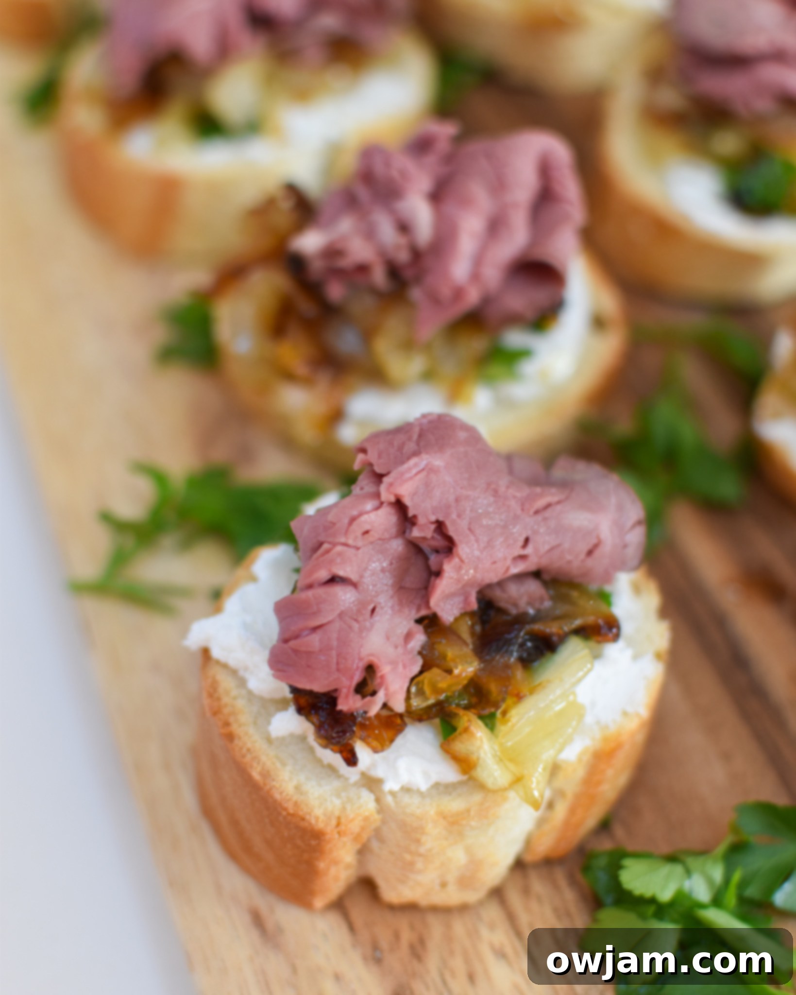 Caramelized Onion Beef Bites 11 Platter of Beef Crostini with Caramelized Onion and Goat Cheese on a rustic cutting board.