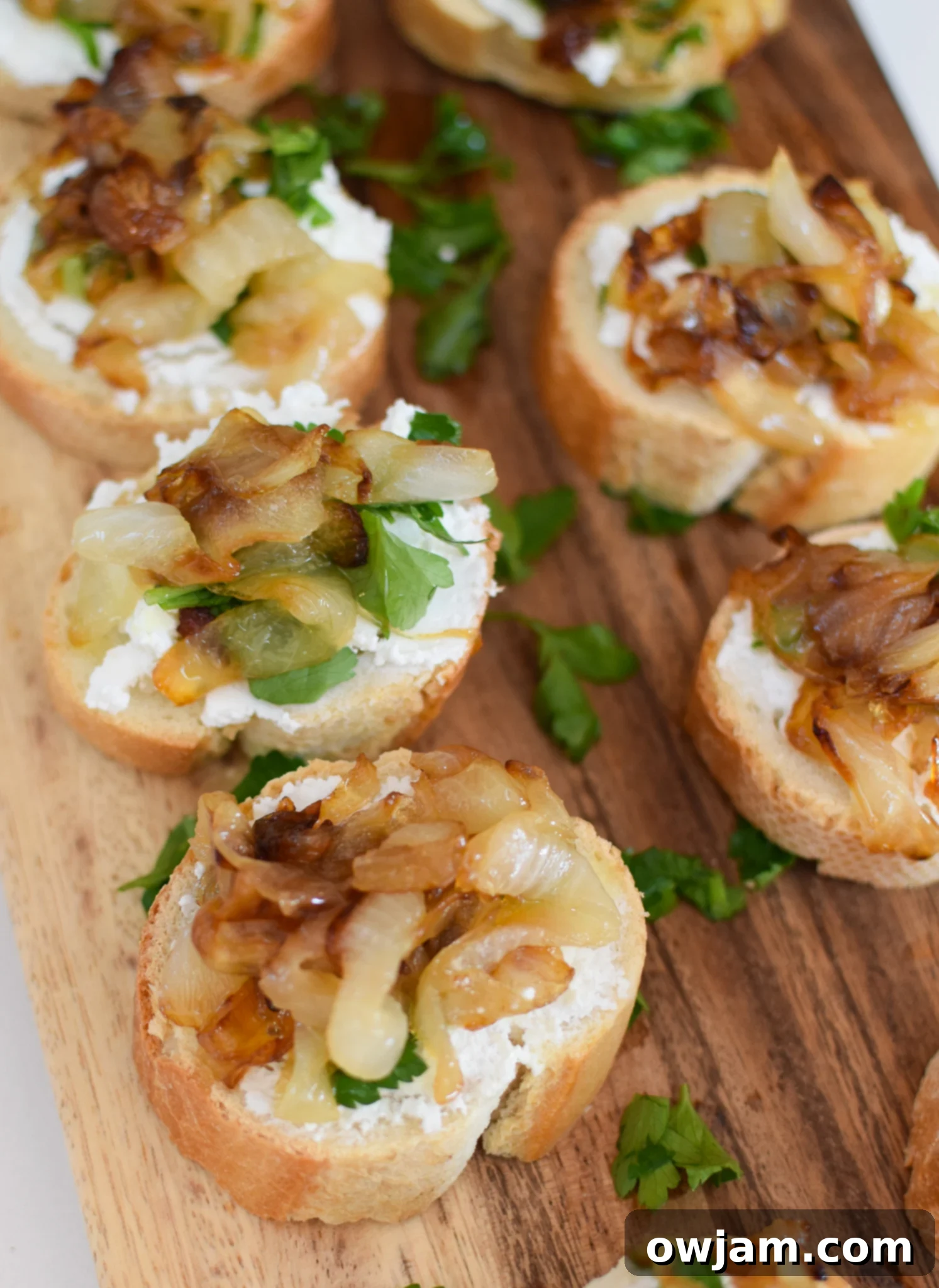 Caramelized Onion Beef Bites 8 Finished Beef Crostini with Caramelized Onion and Goat Cheese on a platter with onions in the background.