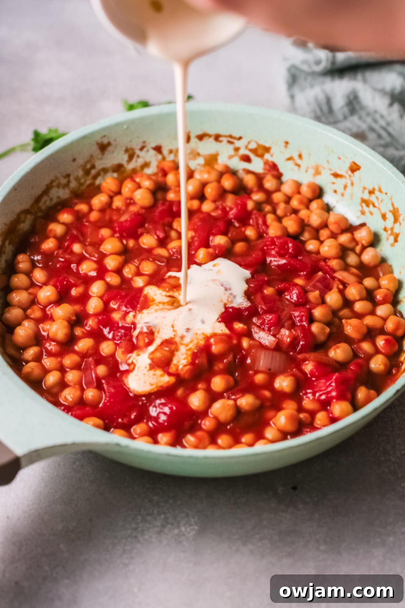 Heavy cream being stirred into the chickpea curry in a pan.