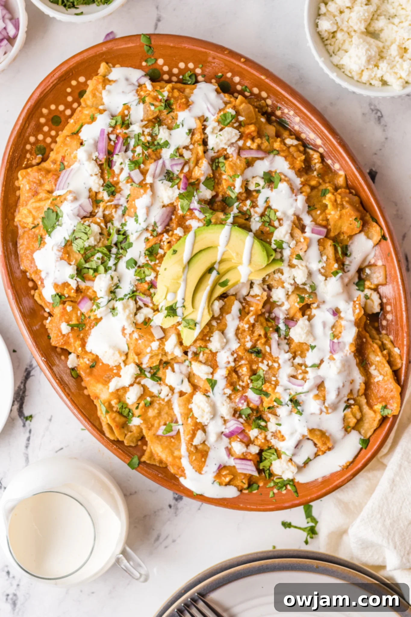 Traditional Red Chilaquiles 3 Chilaquiles Rojos Recipe served in a large platter, generously topped with creamy avocado slices and a swirl of Mexican crema.