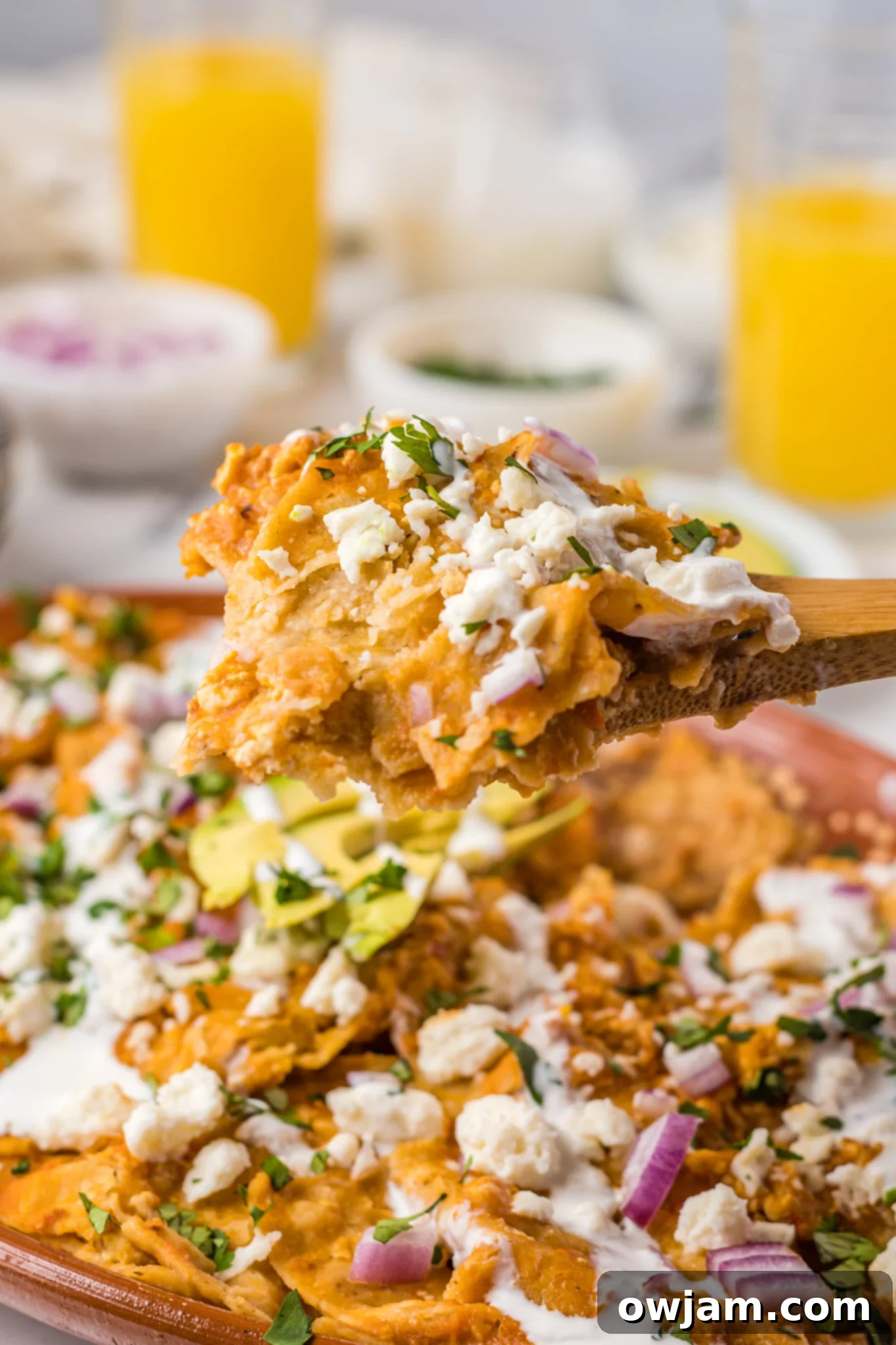 Traditional Red Chilaquiles 5 A wooden spoon scooping up Chilaquiles Rojos, showing chips coated in red sauce and melted cheese.