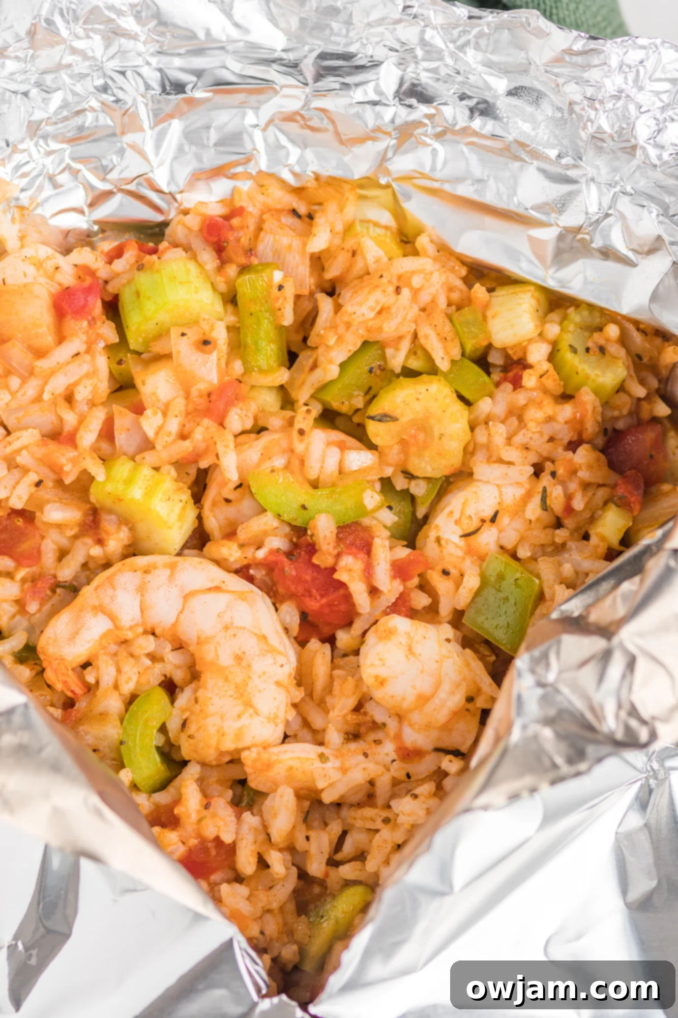 Open foil packet revealing cooked Shrimp Creole garnished with green onions and hot sauce.