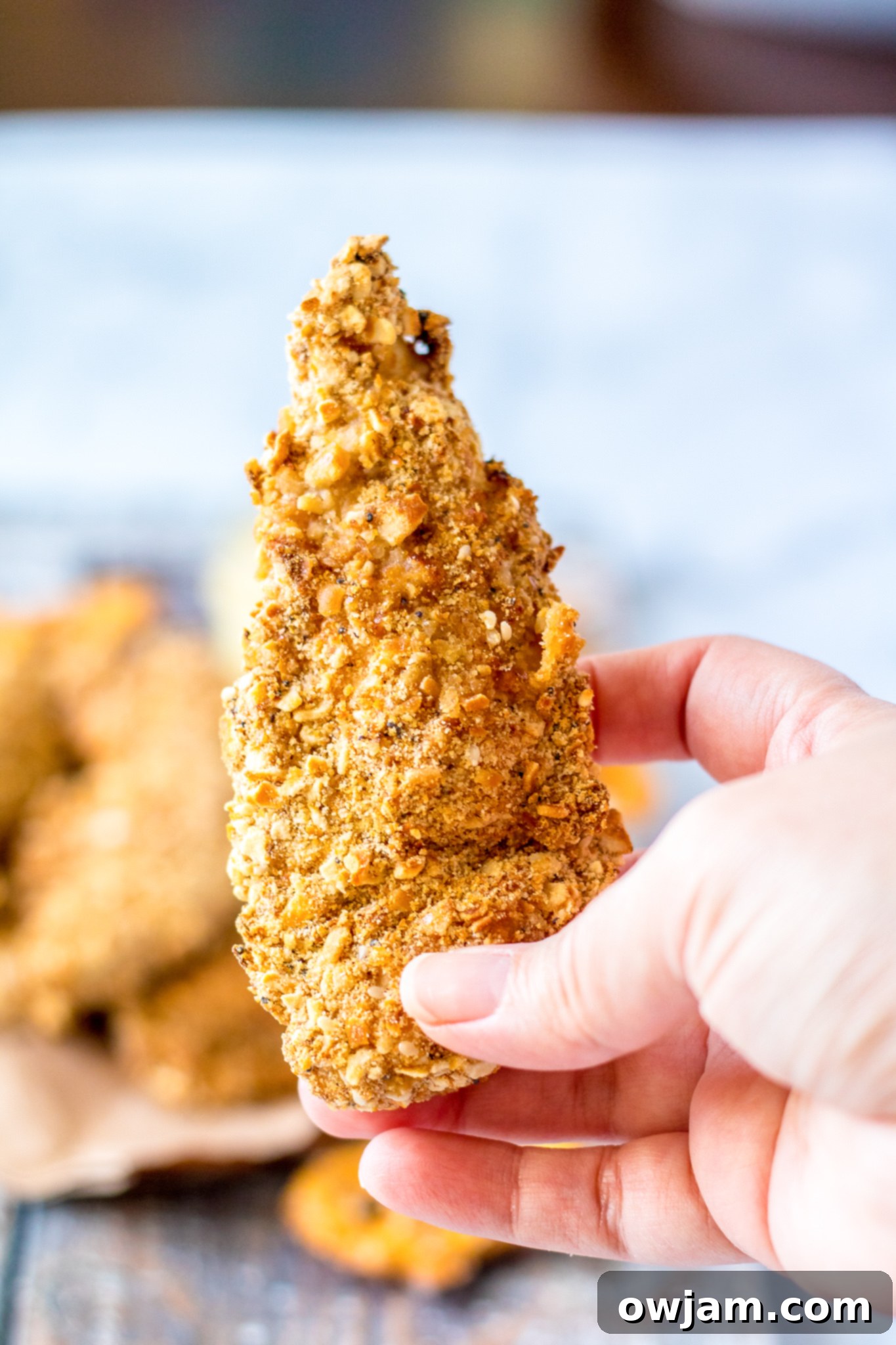 Crunchy Pretzel Chicken 8 A hand reaching for a piece of Pretzel Crusted Chicken tender.