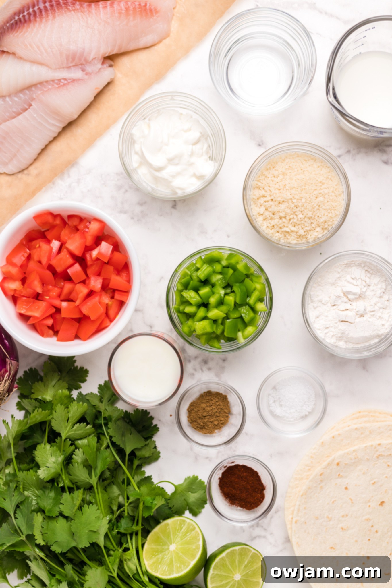 Fresh ingredients for Tilapia Fish Tacos, including tilapia fillets, lime, cilantro, and tomatoes.