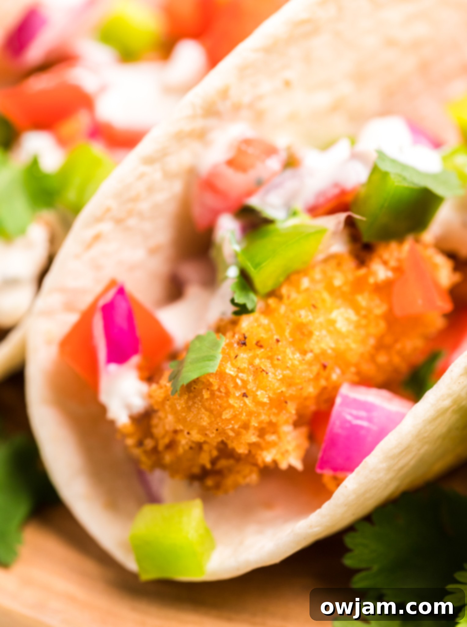 Close-up of a Tilapia Fish Taco garnished with diced tomato and cilantro.