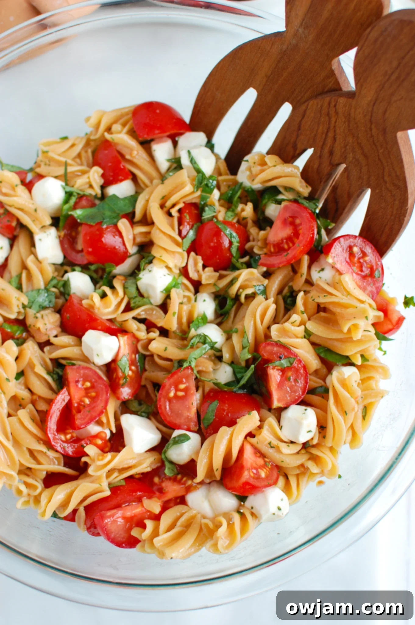 Caprese Pasta with wooden tongs.