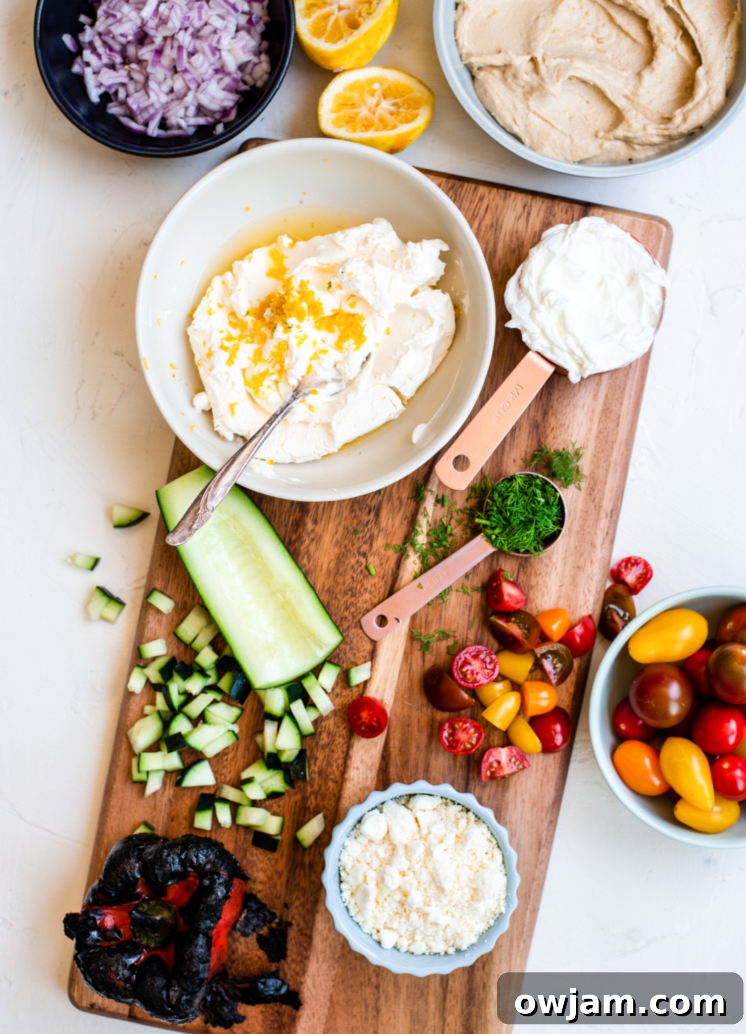 Fresh ingredients laid out for making Layered Greek Dip: Greek yogurt, hummus, vegetables, feta.