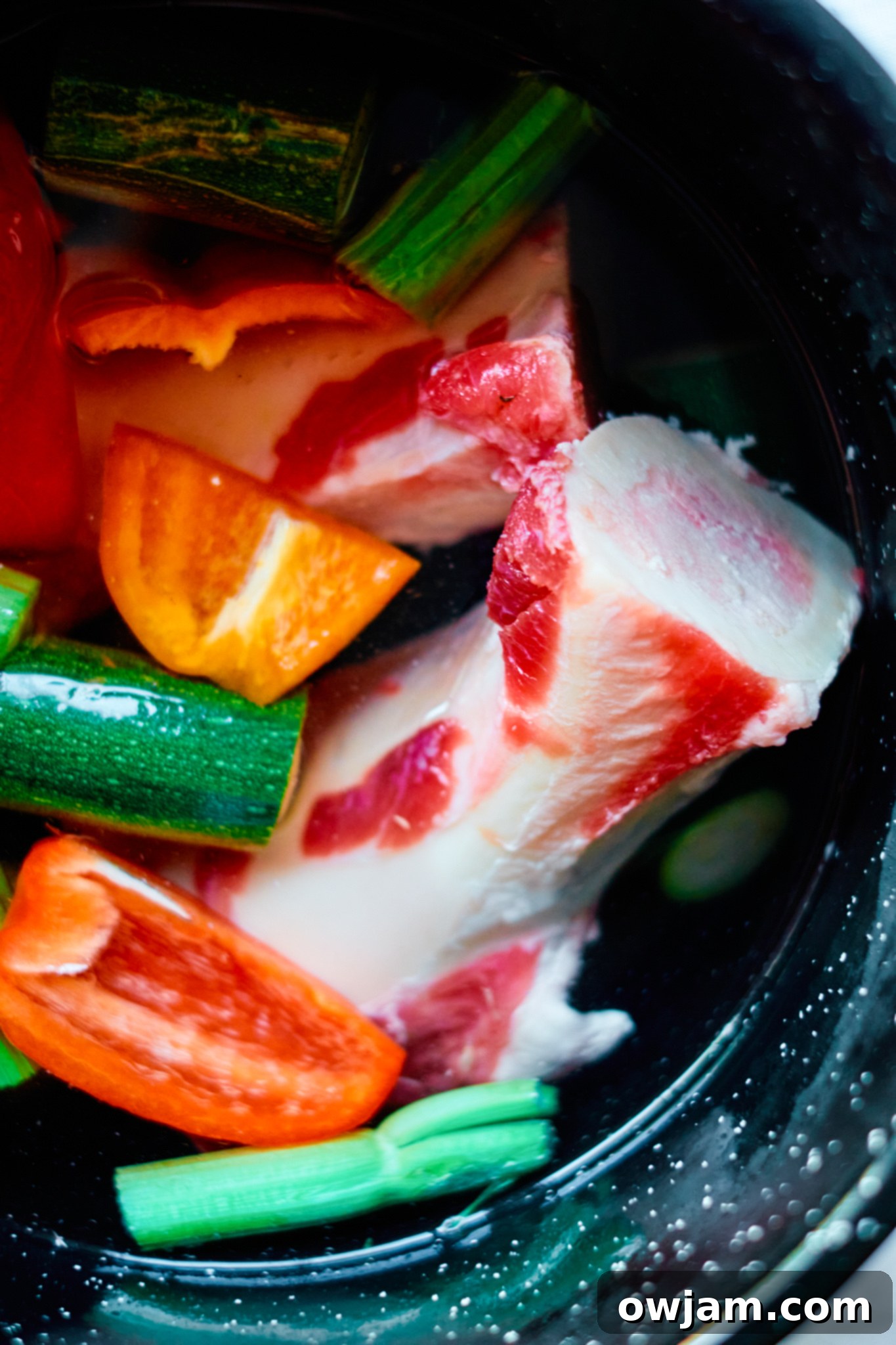 Effortless Homemade Beef Bone Broth 3 Raw beef bones and a selection of fresh vegetables like carrots, celery, onion, ginger, and garlic, prepared for simmering in a large pot.