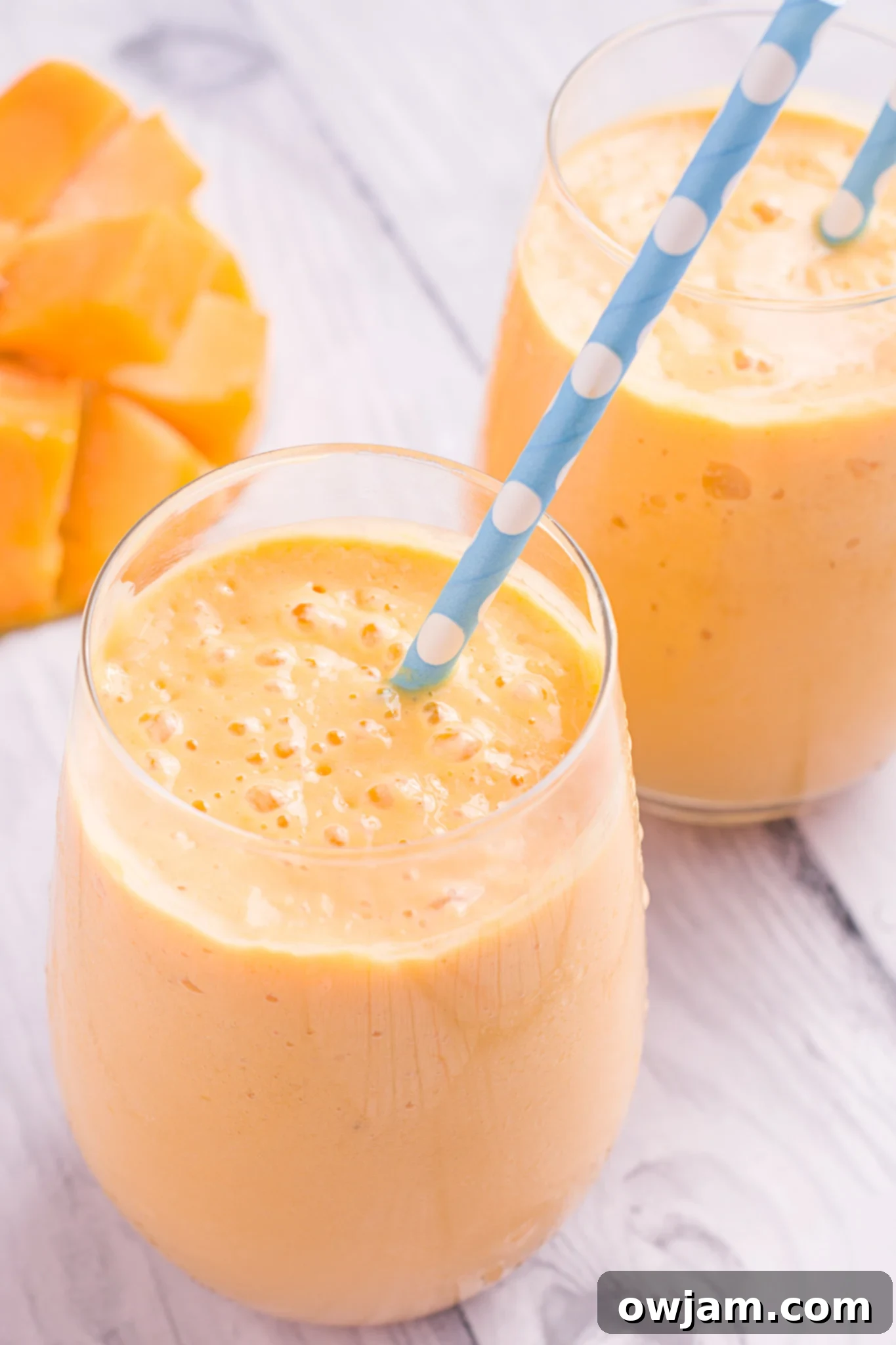 Creamy Mango Lassi Recipe served in a tall glass with a straw, garnished with mint.
