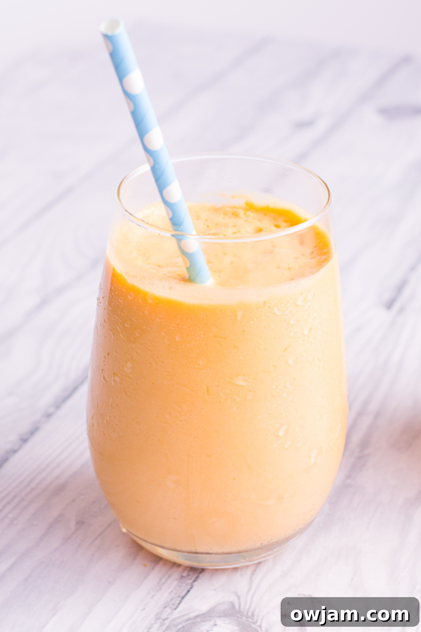 Mango Lassi served in a glass with a straw, garnished with a mango slice.