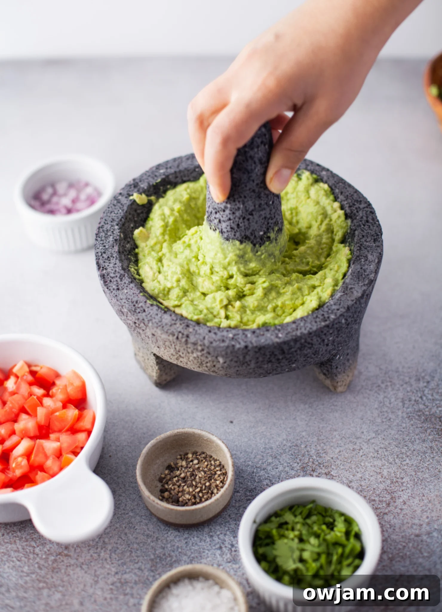 Adding minced red onion and cilantro to mashed avocados in a bowl for Easy Guacamole.