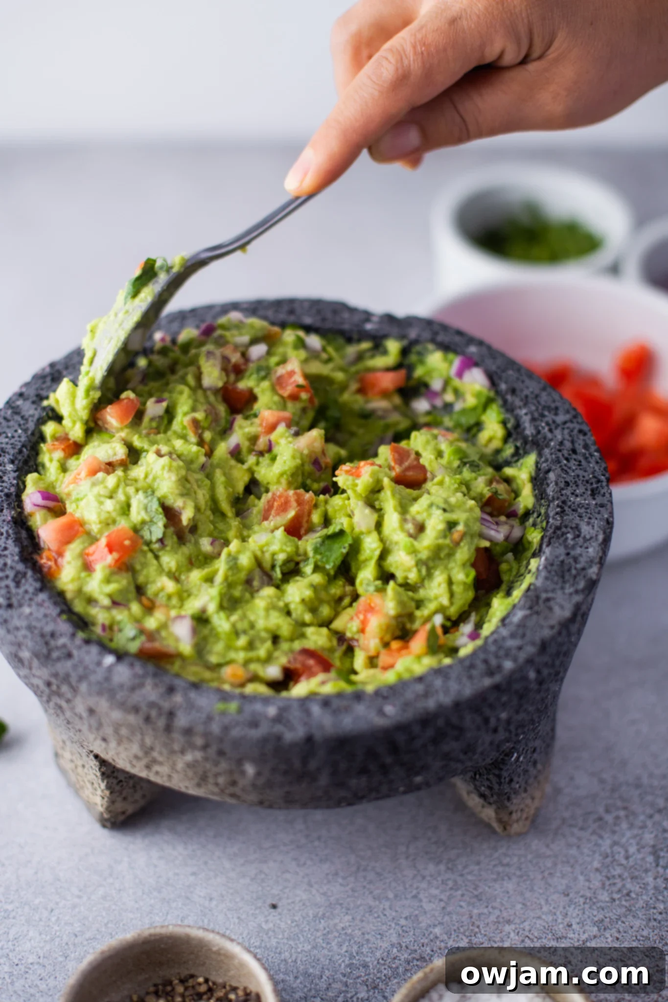 Adding diced jalapeños to the Easy Guacamole mixture with a spoon.