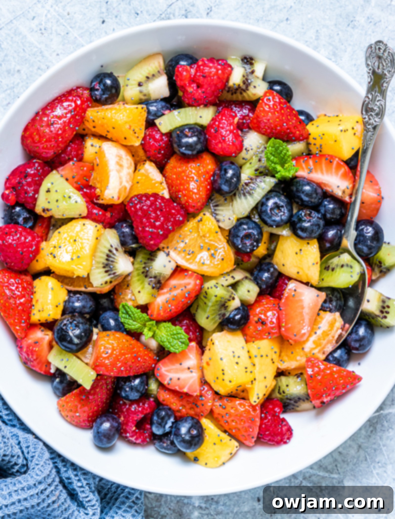 A vibrant fruit salad with lemon poppy seed dressing served in a large bowl, with a spoon ready to scoop.