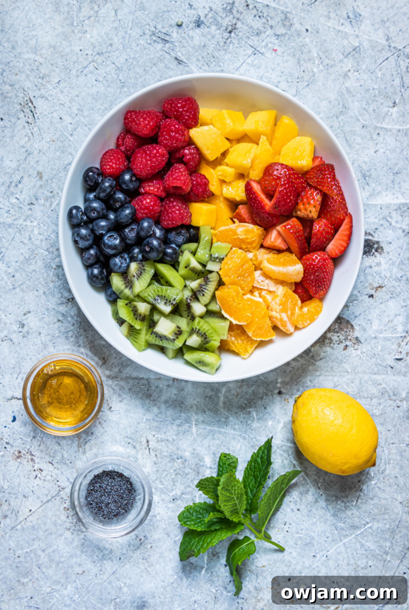 Close-up of fresh fruit ingredients for the lemon poppy seed dressing fruit salad, including strawberries, blueberries, kiwi, mango, and orange.