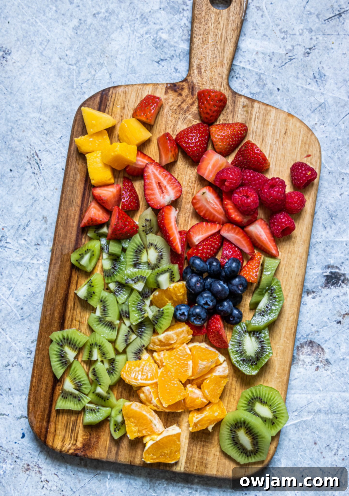 Freshly chopped fruits for fruit salad with lemon poppy seed dressing on a wooden cutting board.