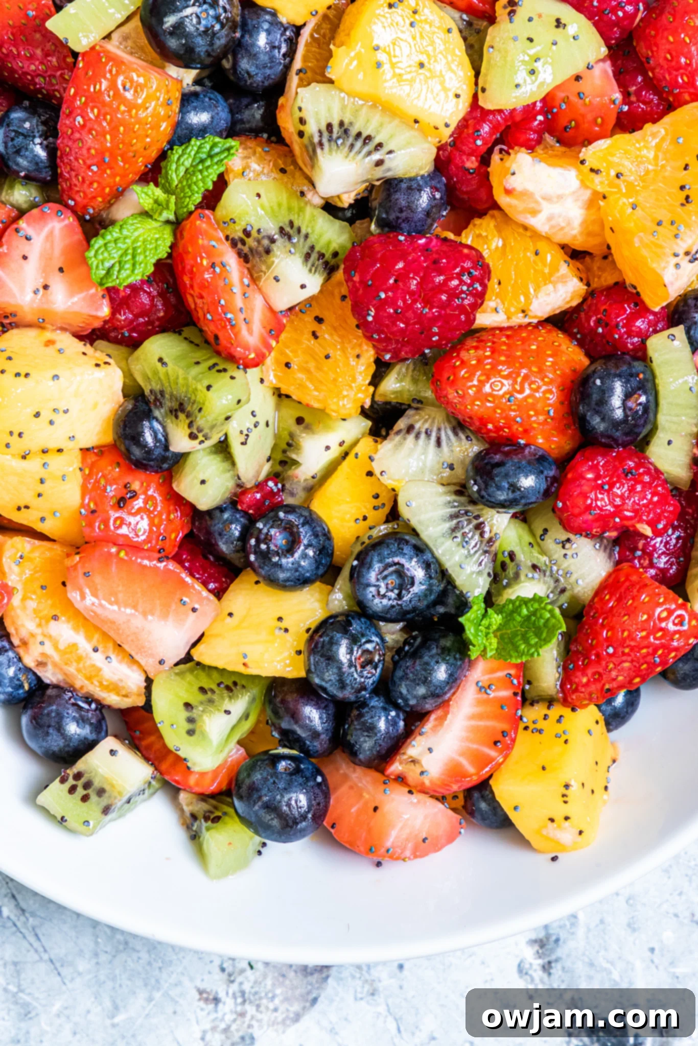 A fruit salad with lemon poppy seed dressing served in a clear glass bowl, garnished with fresh mint.