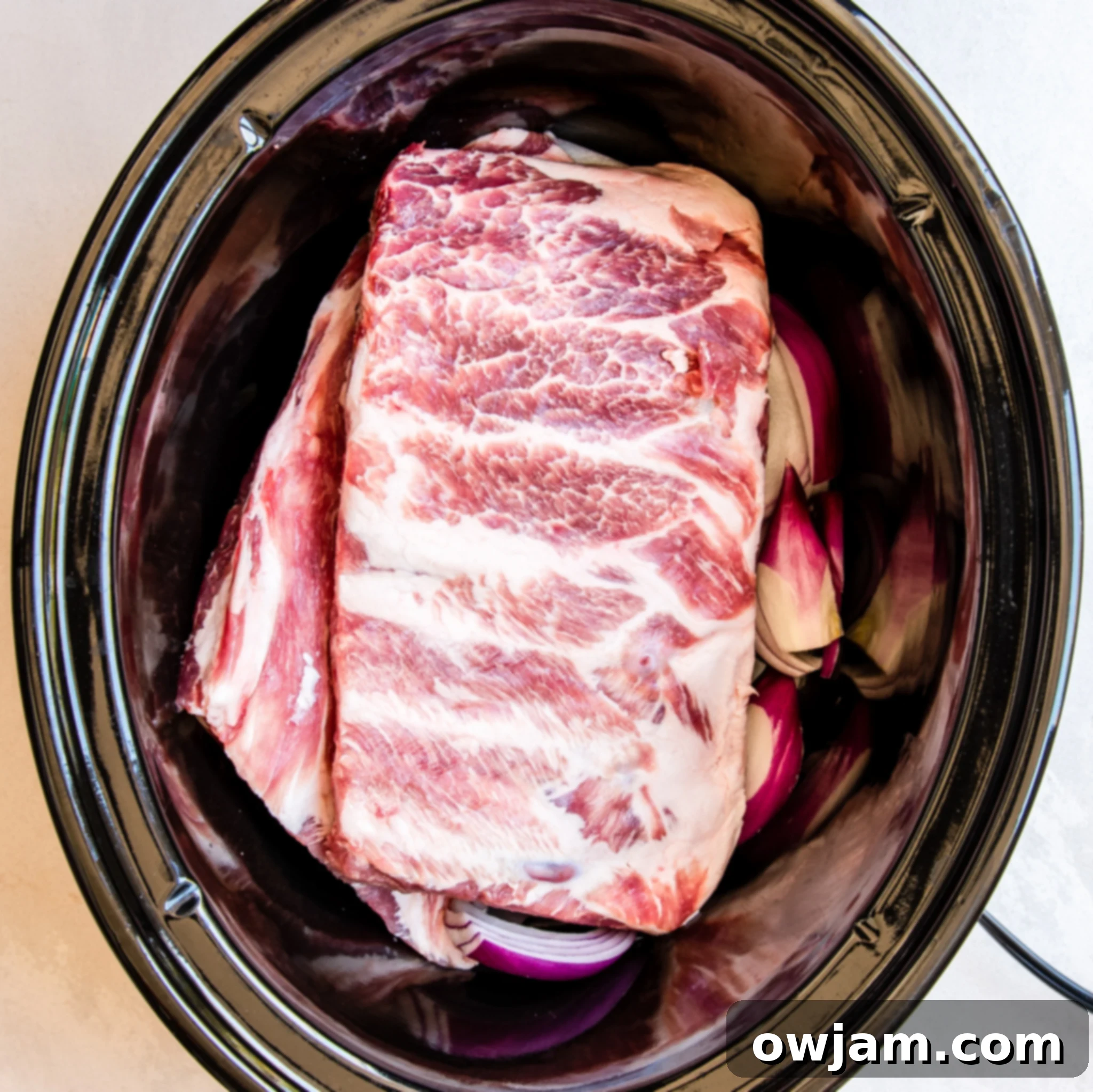 Aloha Slow Cooker Pork Ribs 5 Slow Cooker Hawaiian Pork Ribs placed inside a crockpot on a bed of onions.