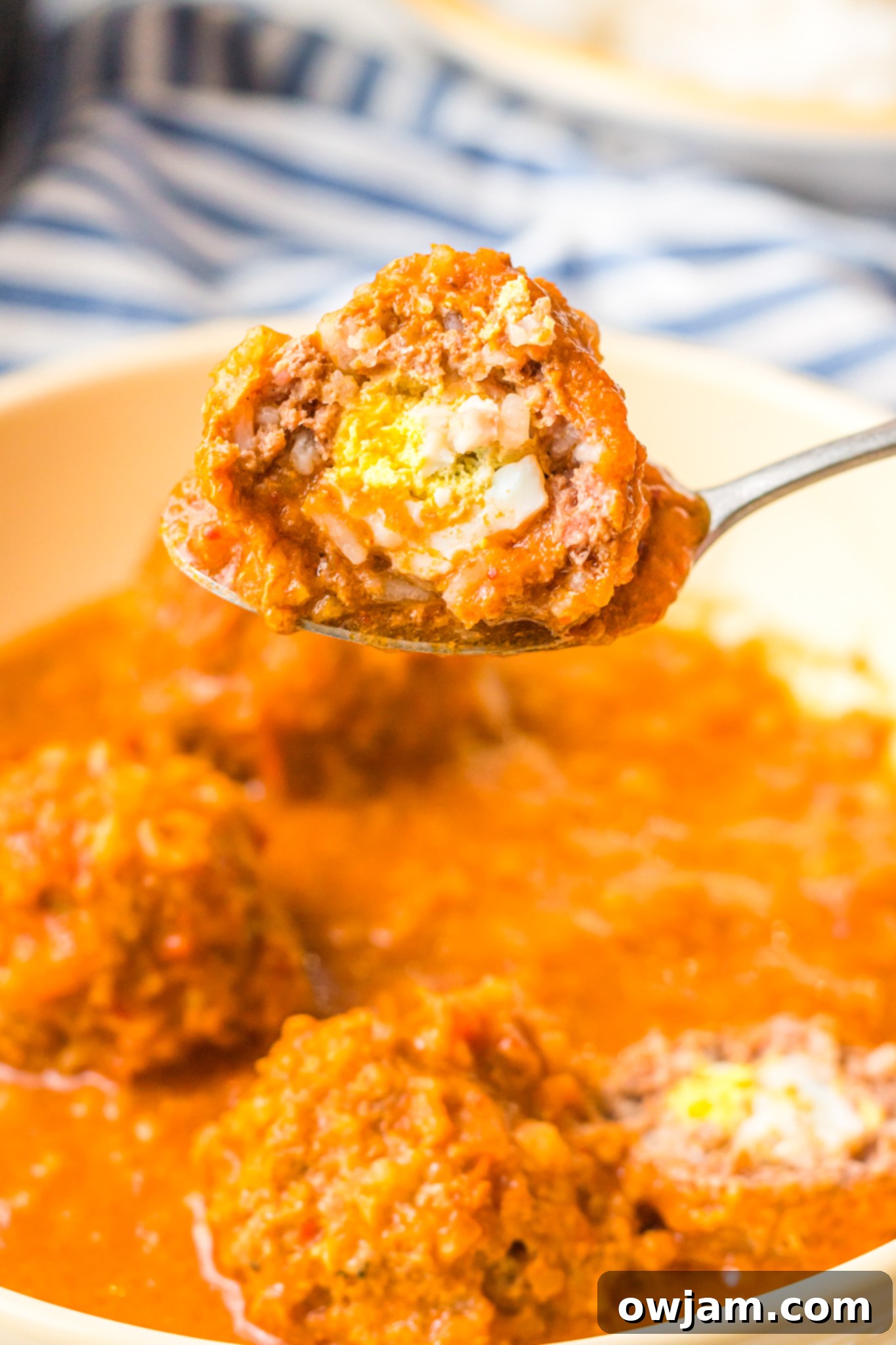 Chipotle Meatballs 2 Delicious Albondigas en Chipotle, a Mexican meatball dish, served with rice. One meatball is held on a spoon, revealing the hard-boiled egg inside, garnished with fresh cilantro.