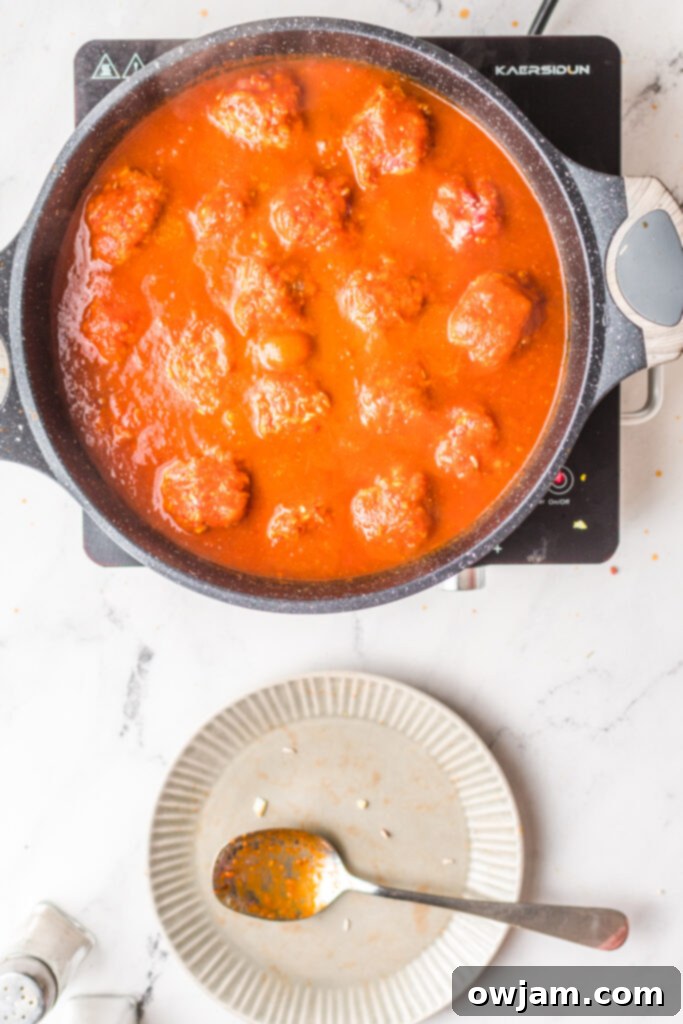Chipotle Meatballs 11 Albondigas en Chipotle meatballs gently simmering in a rich, red chipotle sauce in a large pot on the stovetop.