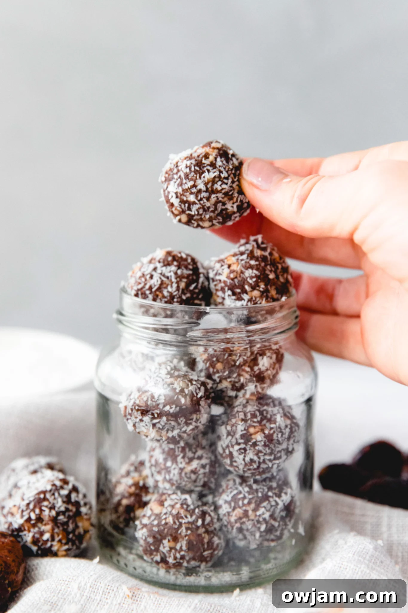 No-Bake Date Energy Bites 9 A hand holding an Easy Date Protein Ball above a jar filled with more protein balls.