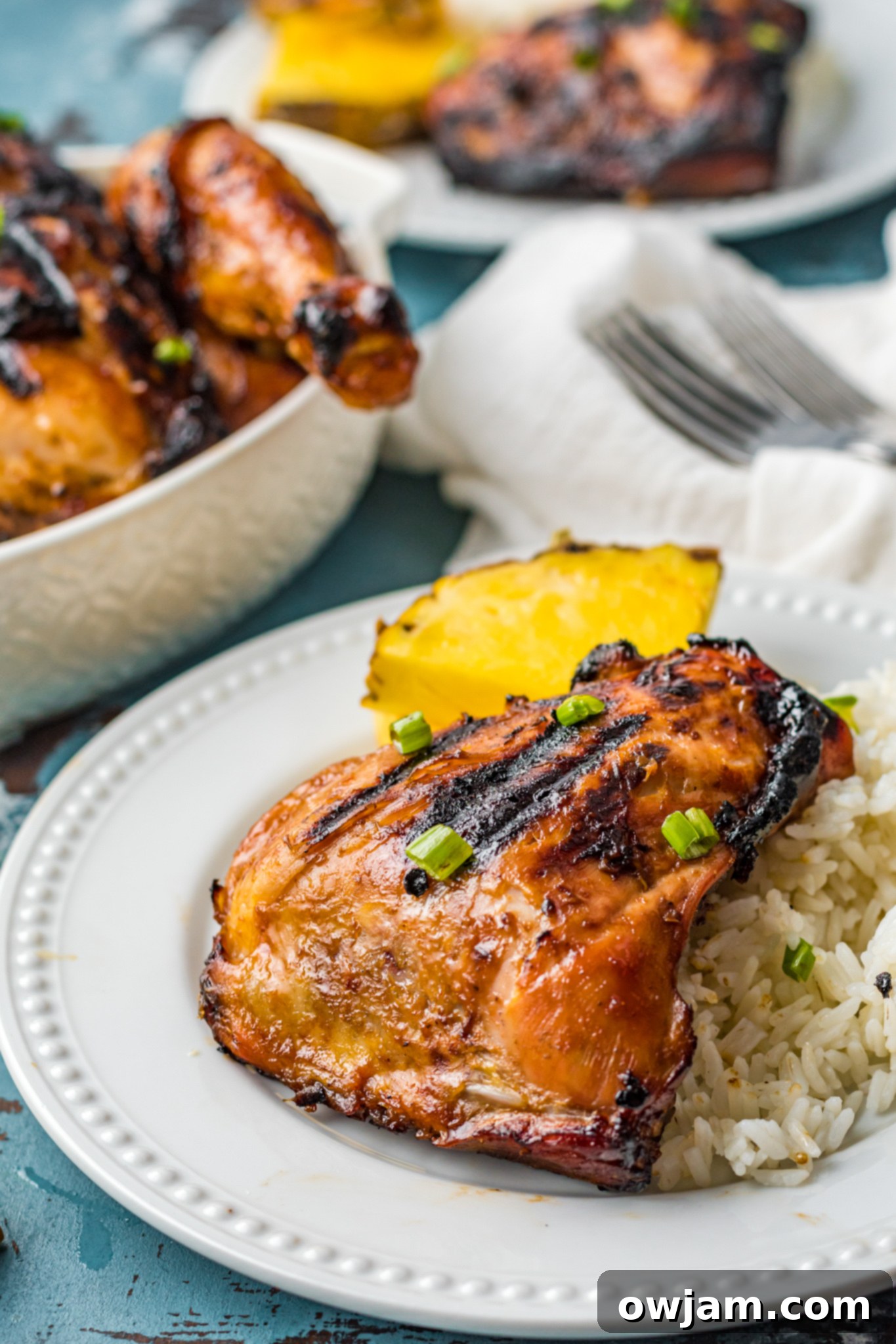 Hawaiian Fire Chicken 2 Grilled Huli Huli Chicken on a white plate, garnished with fresh herbs and a slice of lime. The chicken is beautifully caramelized.