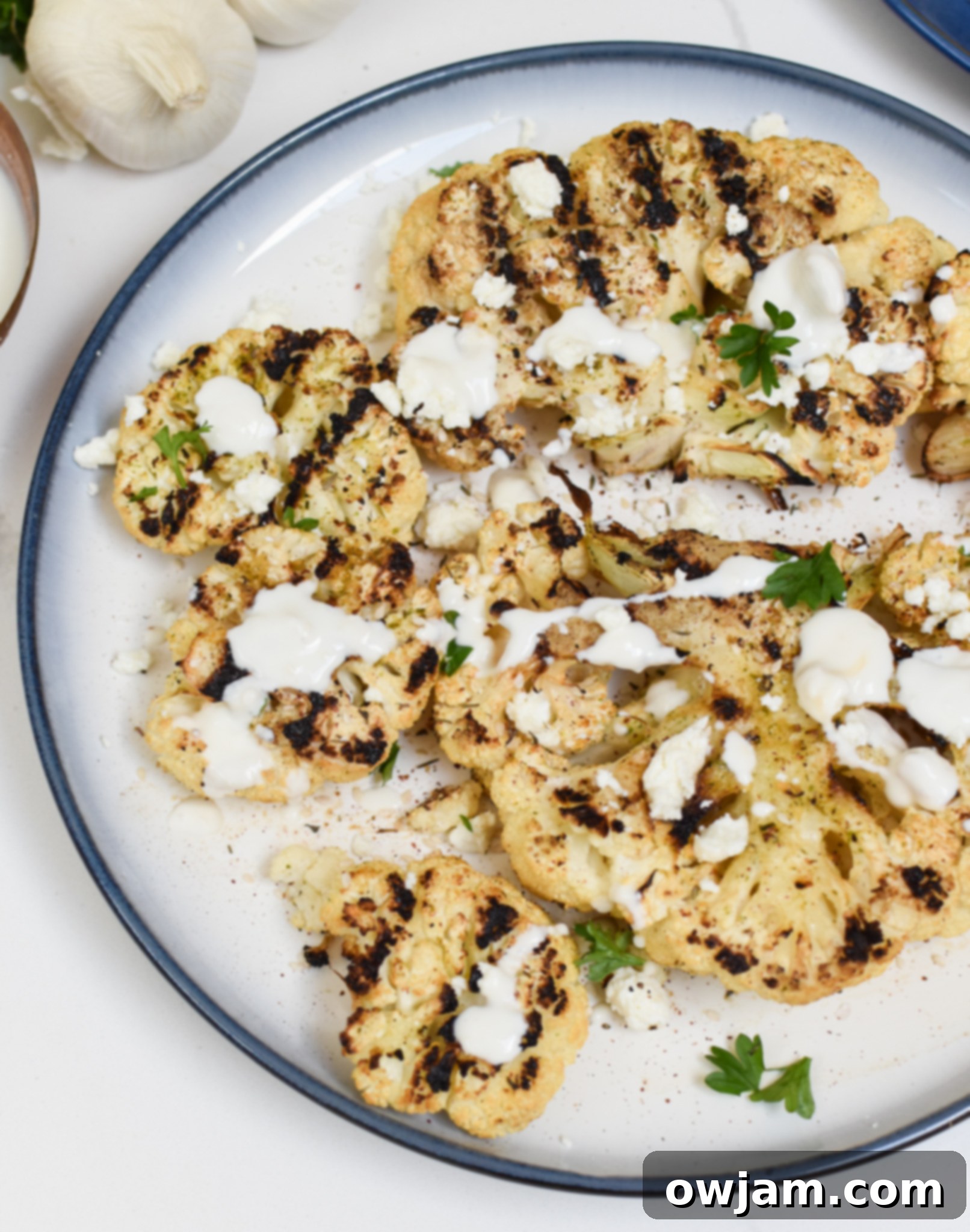 Grilled Cauliflower Steaks with Yogurt Tahini Sauce on a white plate, garnished with fresh herbs and feta.