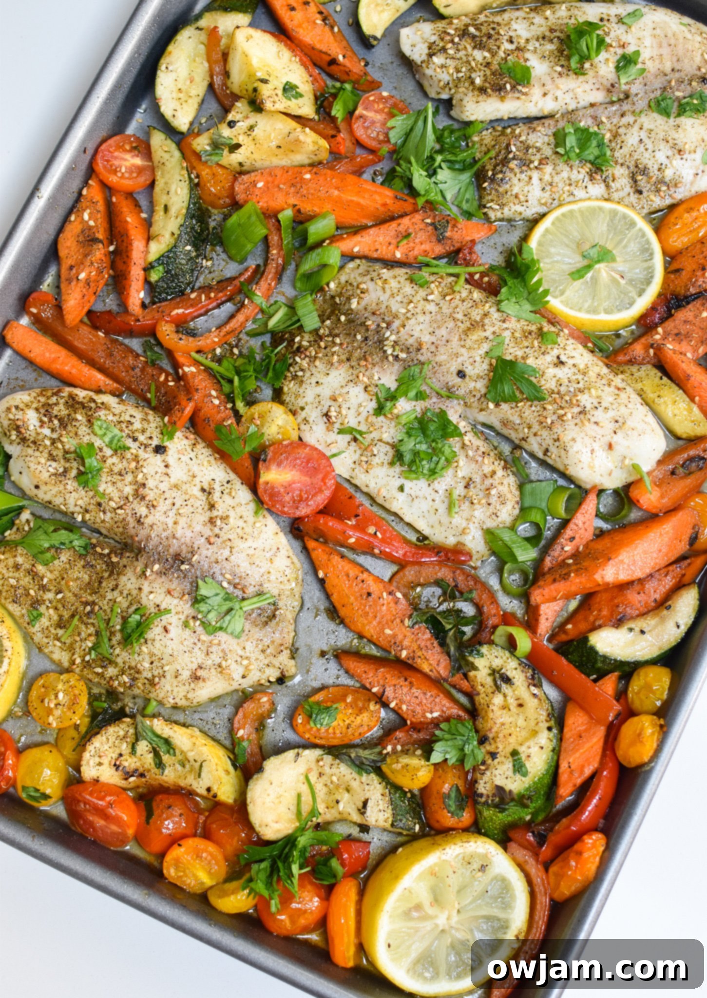 Golden Mediterranean Tilapia Bake 2 Mediterranean Baked Tilapia on a sheet pan with a vibrant assortment of vegetables and fresh herbs, ready to be served.
