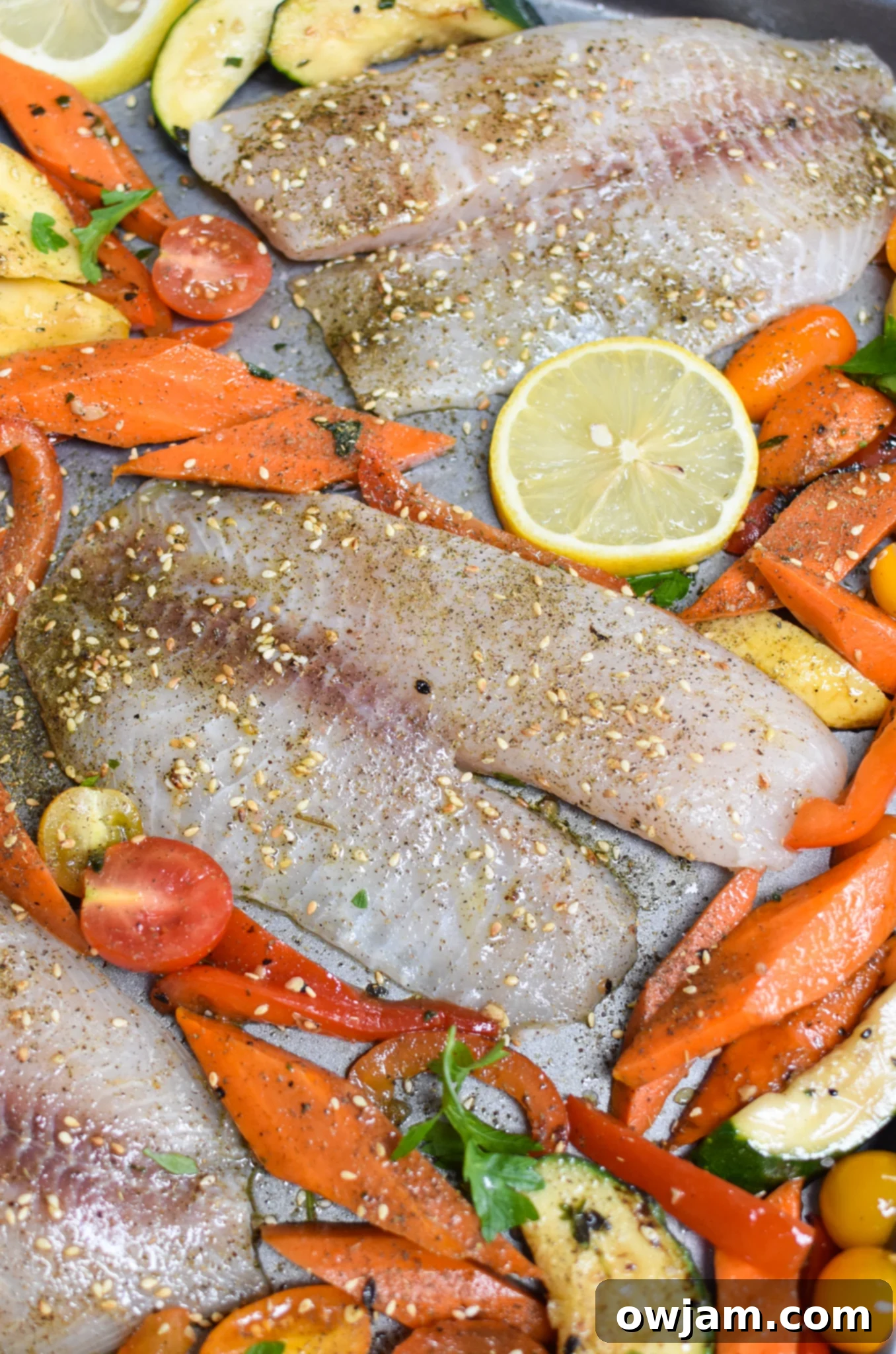 Golden Mediterranean Tilapia Bake 5 Uncooked Mediterranean Baked Tilapia fillets nestled among colorful, seasoned vegetables on a sheet pan, ready for the oven.