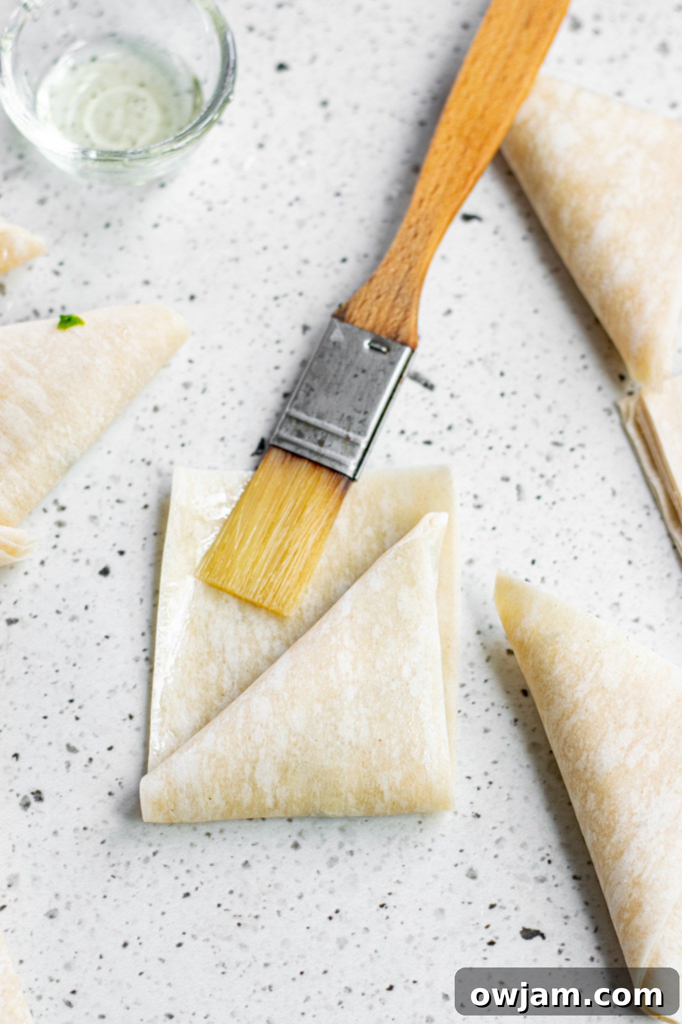 Crispy Spanakopita Pastries 6 Phyllo dough strips for Spanakopita Triangles Recipe being brushed with melted butter.