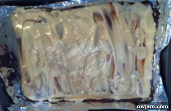 Melted white chocolate poured over a hardened dark chocolate layer, ready for peppermint topping to make festive bark.
