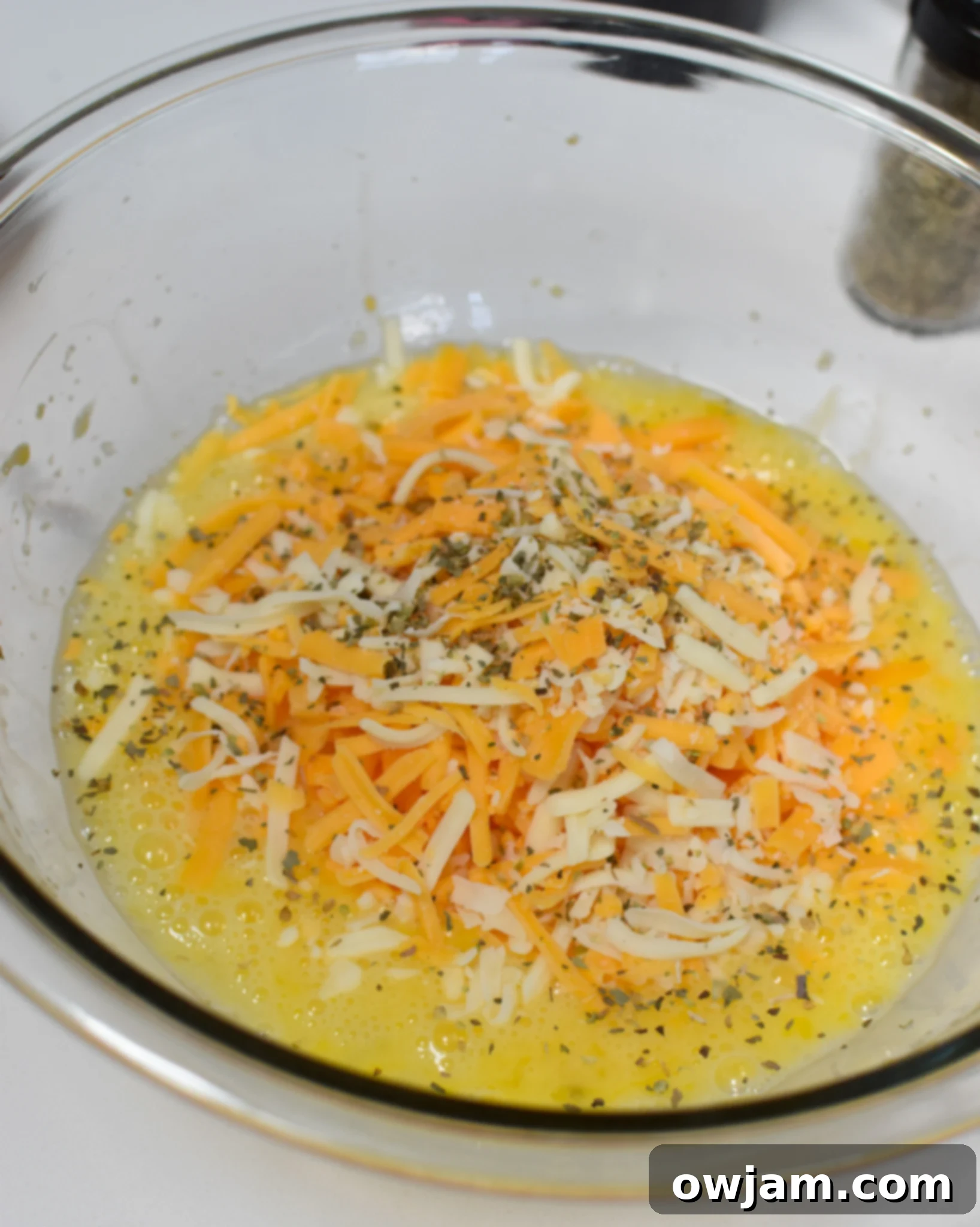 Bowl with whisked eggs and shredded cheese, along with spices and chives, ready to be mixed for the Chaffles Recipe.