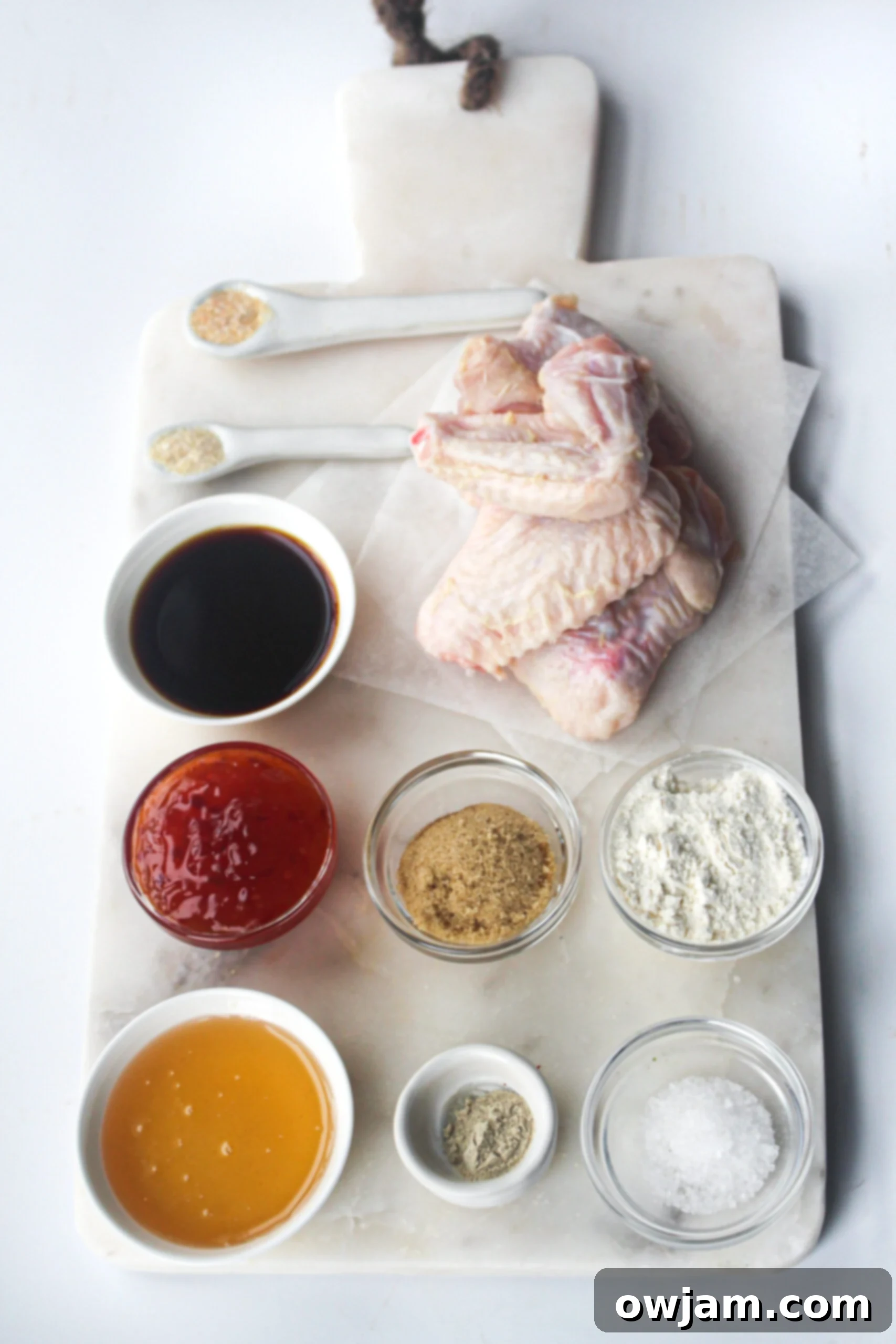 Collection of fresh ingredients for Air Fryer Chicken Wings, including raw chicken wings, spices, honey, brown sugar, sweet chili sauce, and soy sauce on a wooden board.