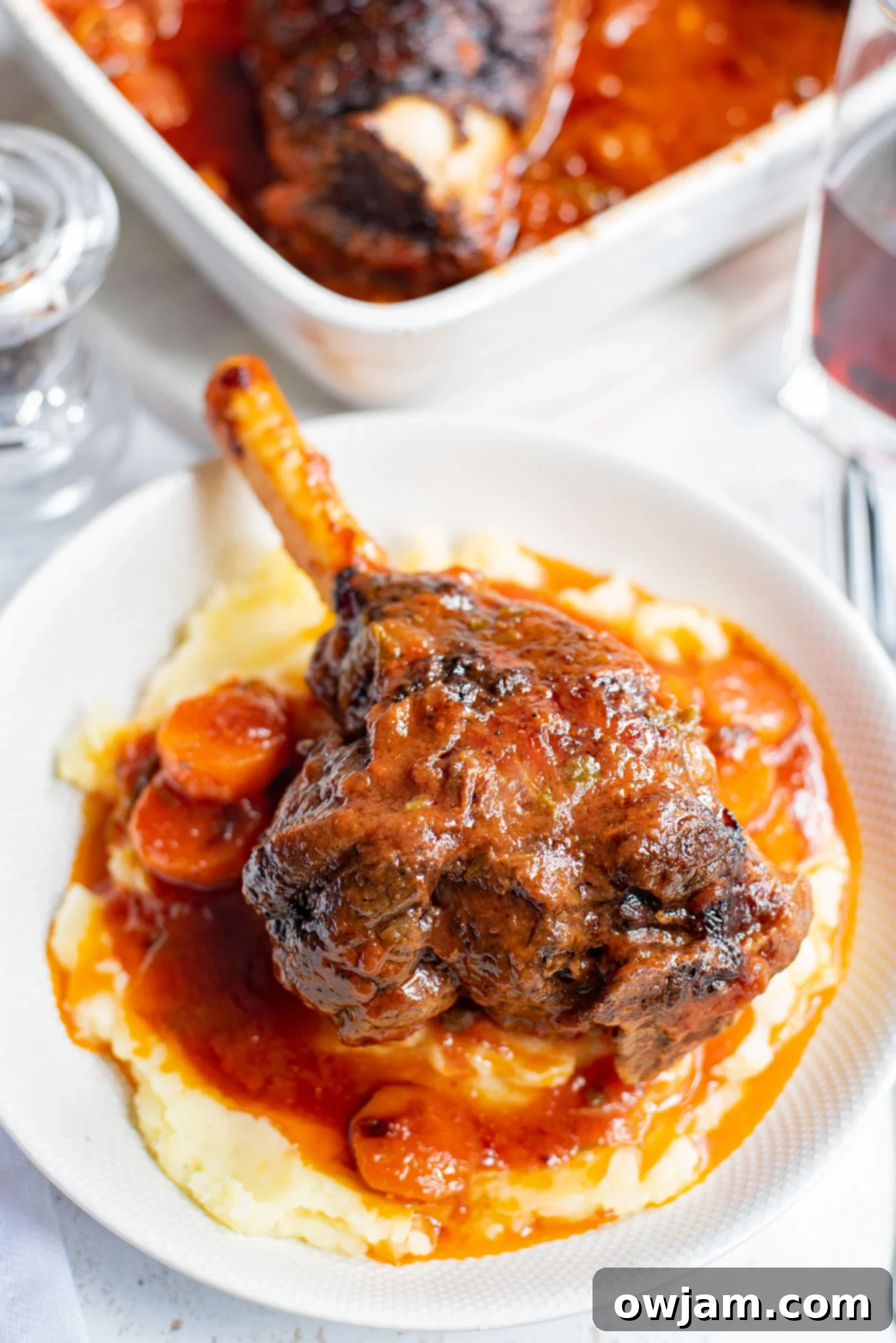 Perfectly braised lamb shank in a white bowl, garnished with fresh herbs.