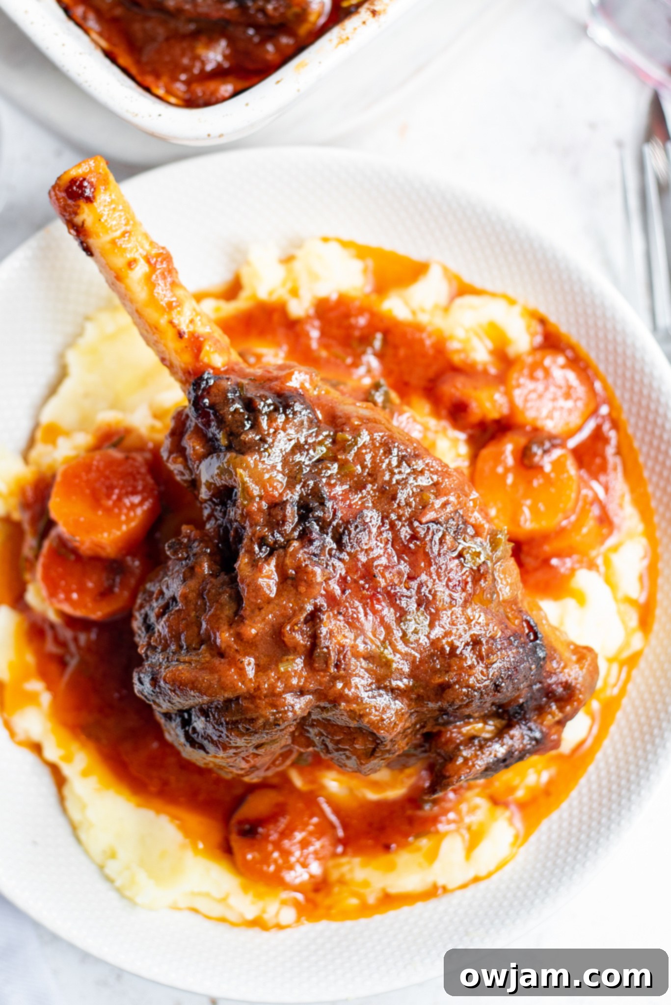 Close-up of braised lamb shanks with tender carrots and rich sauce in a baking dish.