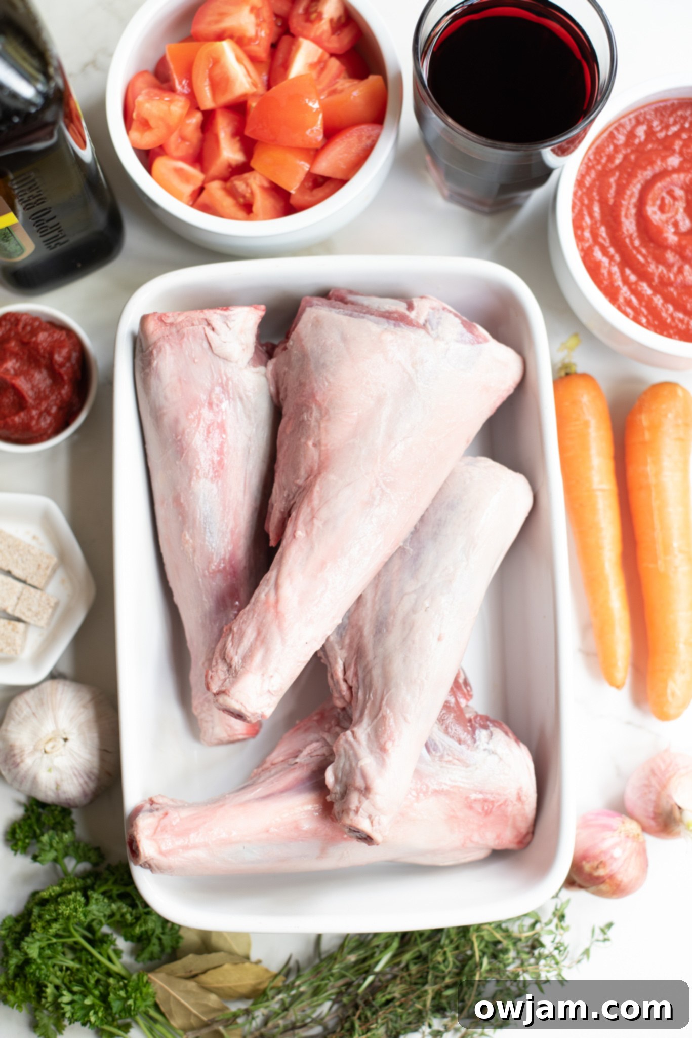 Fresh ingredients laid out for braised lamb shanks recipe, including carrots, tomatoes, onion, and herbs.