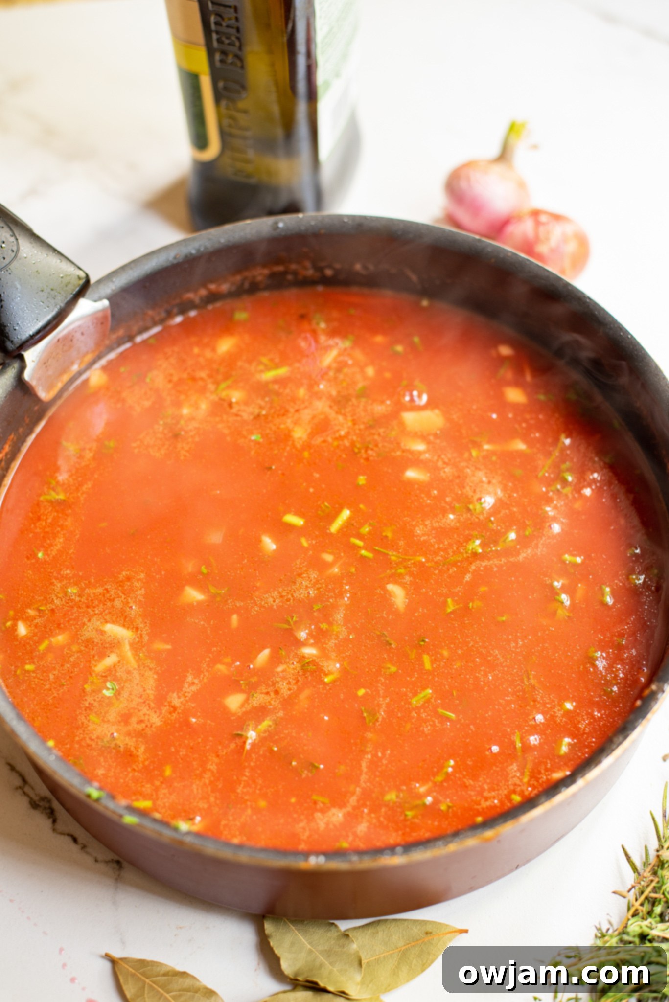 Braising liquid with herbs simmering in a skillet, ready for lamb shanks.
