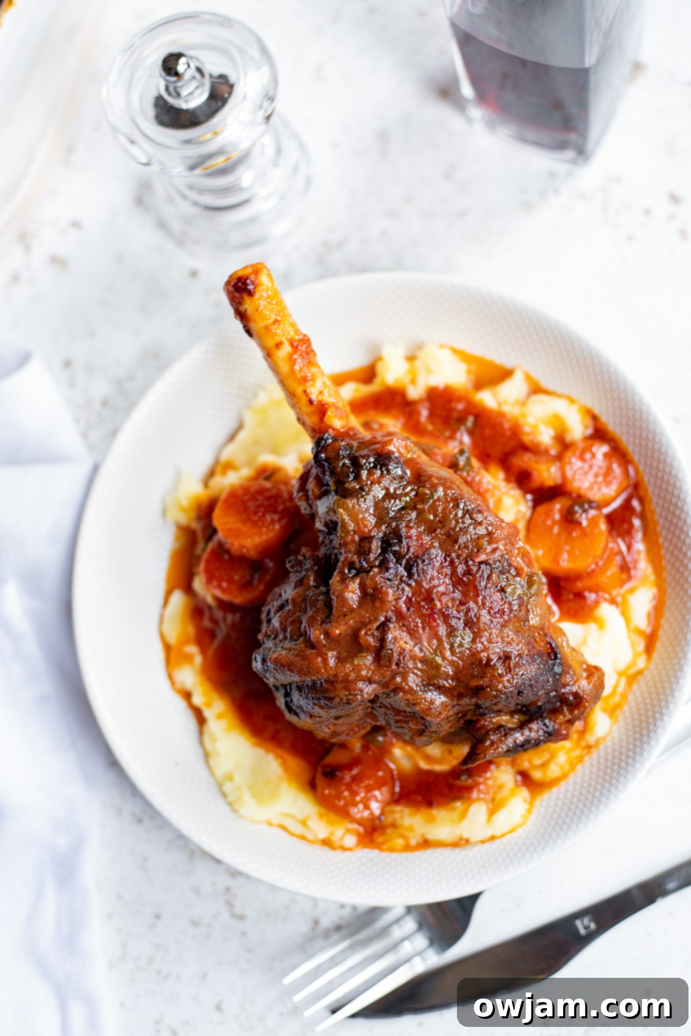 Braised lamb shank served beautifully with mashed potatoes in a white bowl.