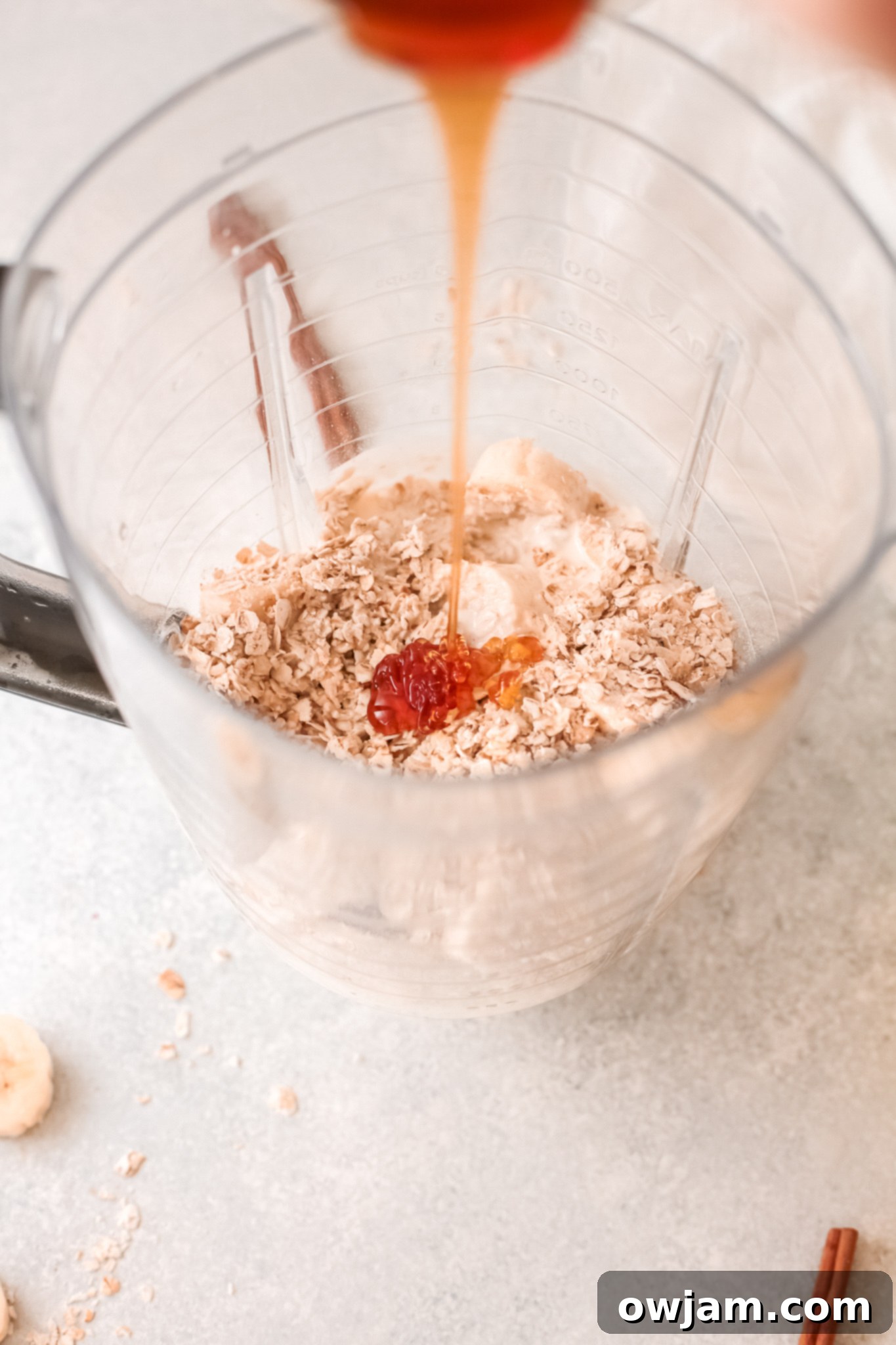 A stream of golden honey being drizzled into a blender full of oat smoothie ingredients, enhancing its sweetness.