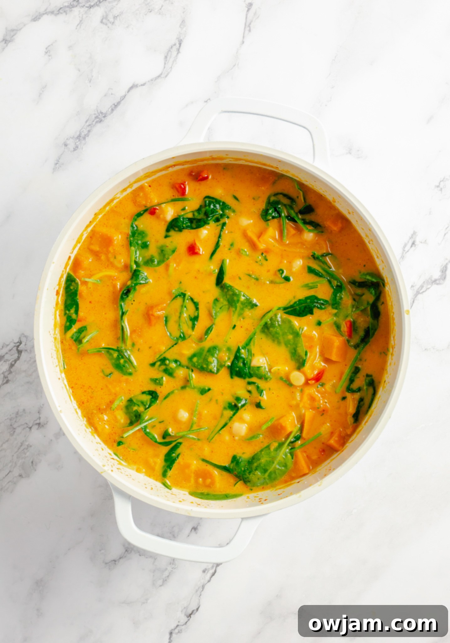 Fresh spinach being added to the simmering Pumpkin Curry Recipe in a pot, adding vibrant green.
