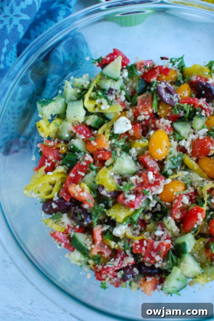 Vibrant Mediterranean Quinoa Salad 6 A large, clear glass bowl filled with vibrant Greek Quinoa Salad, beautifully showcasing its colorful medley of wholesome ingredients and fresh, appealing appearance.