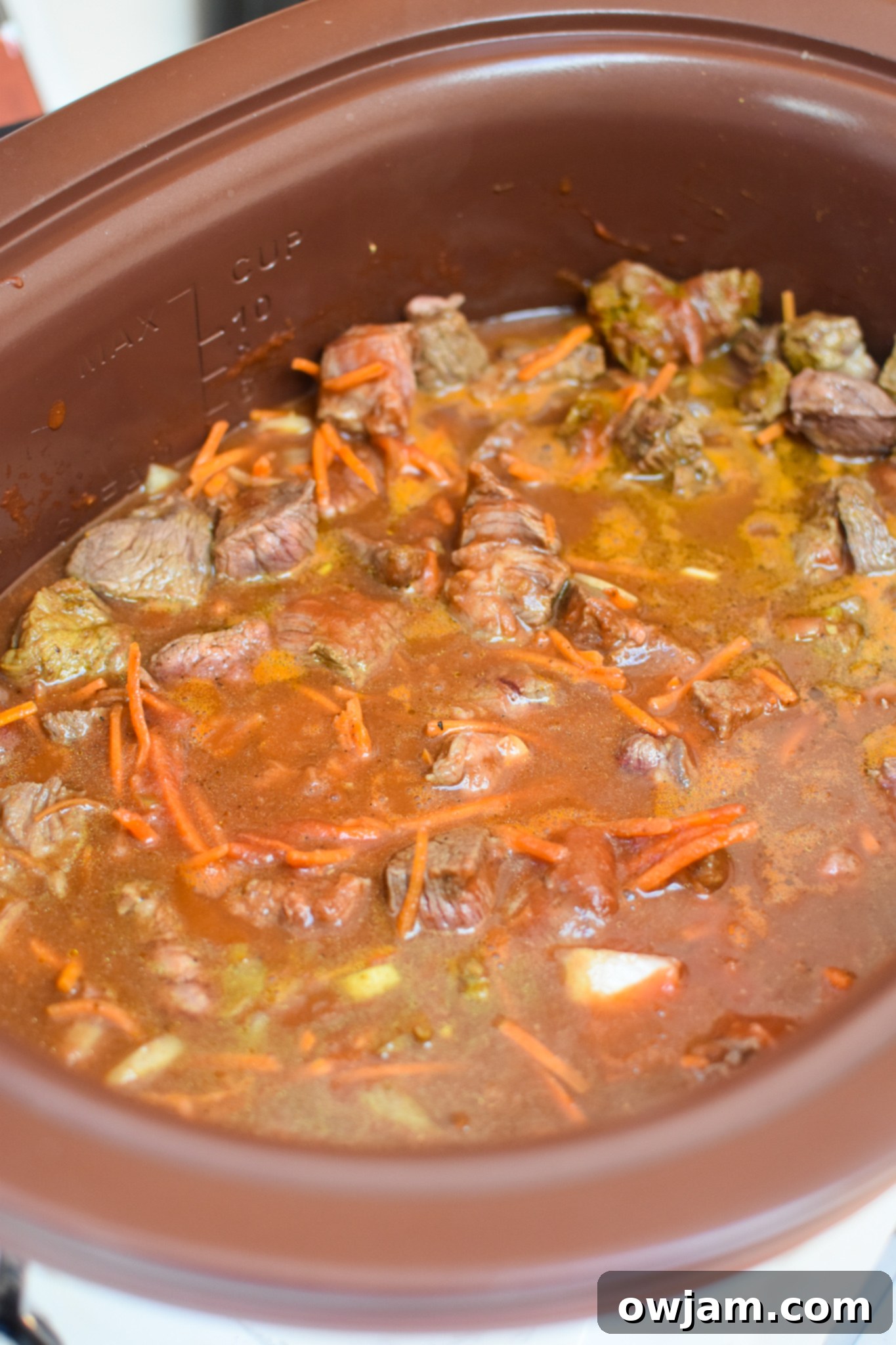All Slow Cooker Beef Curry ingredients, including browned beef, vegetables, and spices, combined in a crockpot before cooking.