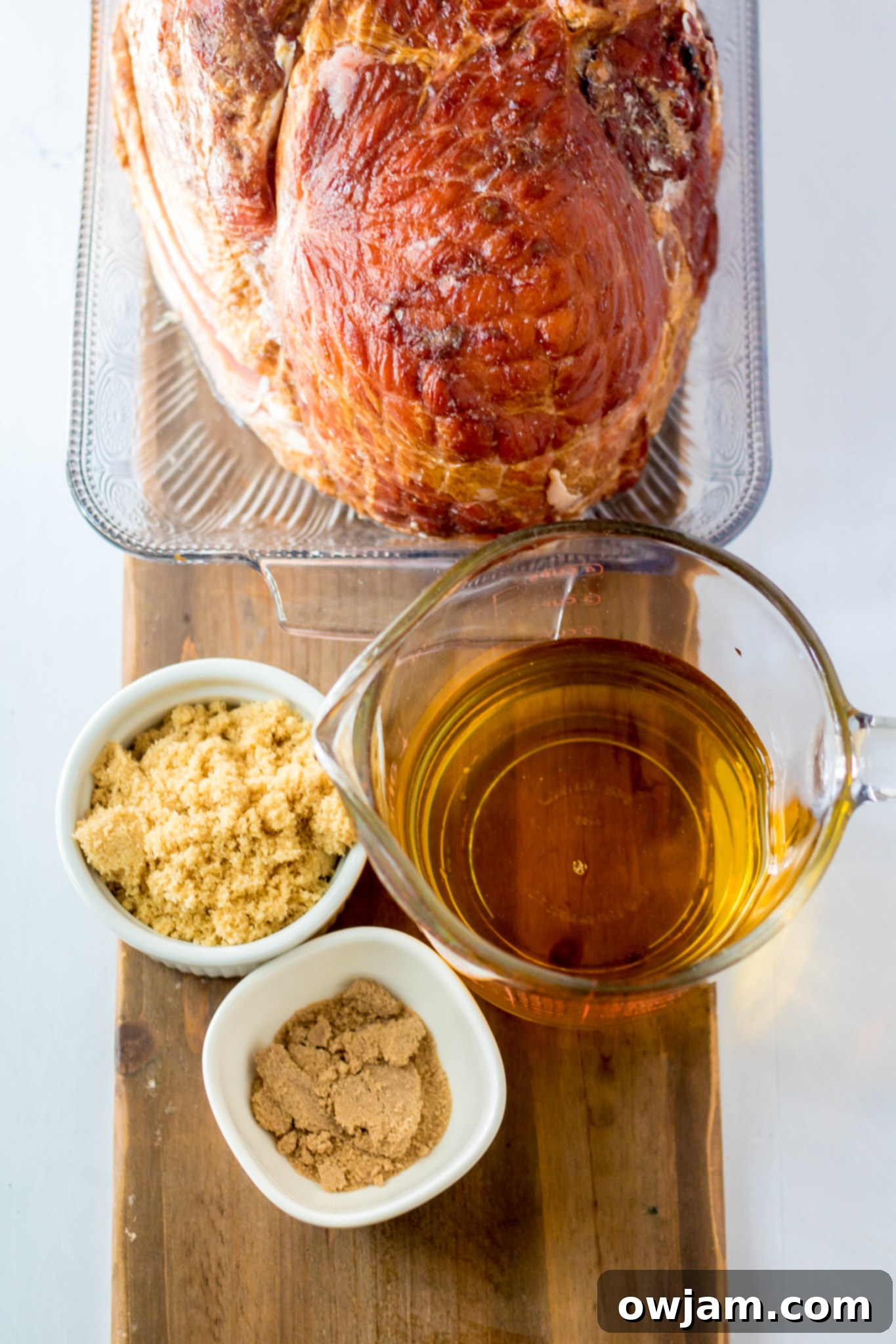 Juicy Apple Cider Glazed Ham Recipe 3 Ingredients for Apple Cider Glazed Ham Recipe laid out on a cutting board, including ham, apple juice, brown sugar, and spiced cider mix.