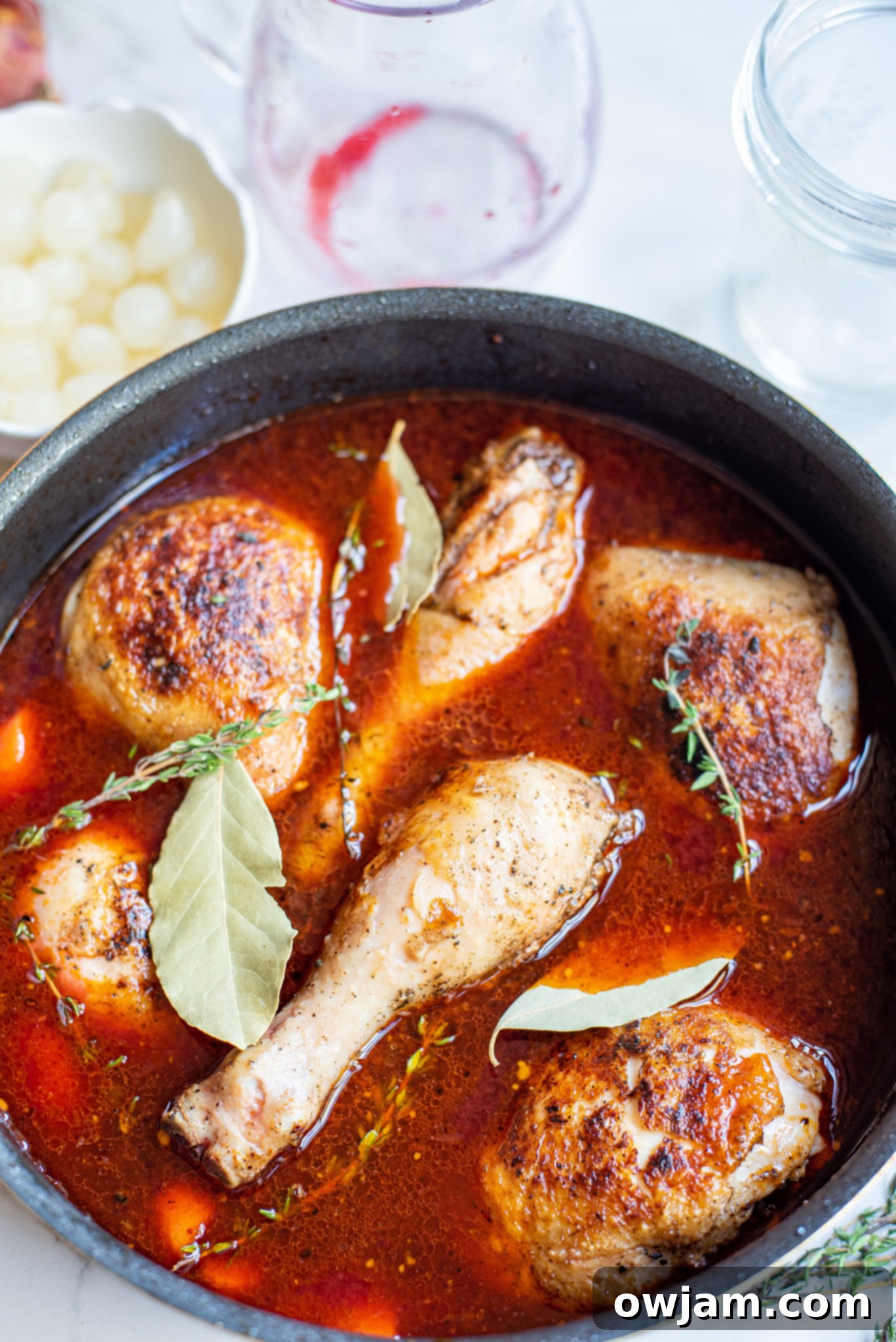 Coq au Vin simmering in a rich, red wine sauce in a Dutch oven, with chicken and vegetables.